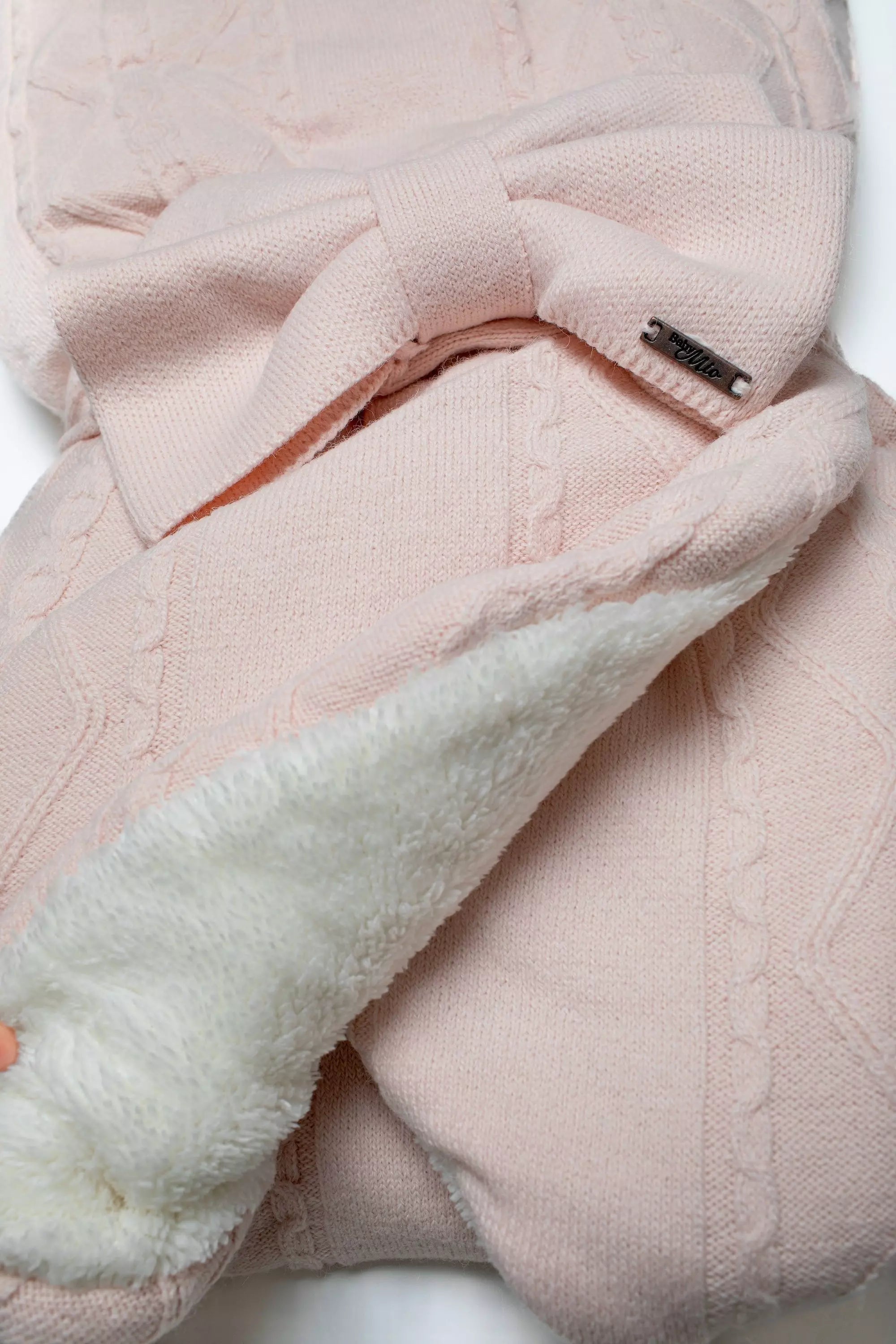 Detailansicht der rosa Strick-Einschlagdecke mit Schleife und Blick auf das weiche, weiße Teddyfutter.