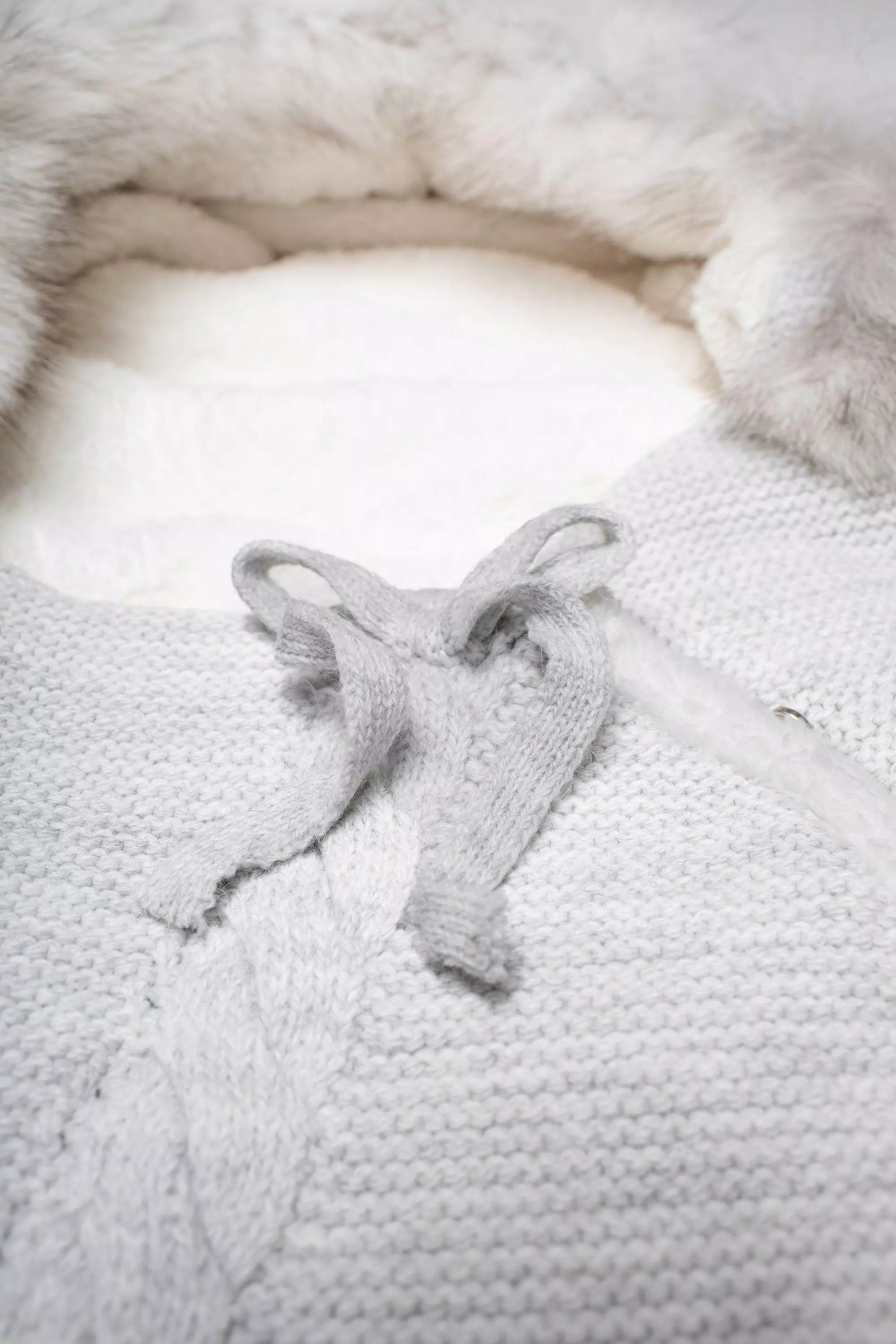 Nahaufnahme des Strick-Baby-Schlafsacks in Grau mit Zopfmuster und Schleifenverschluss