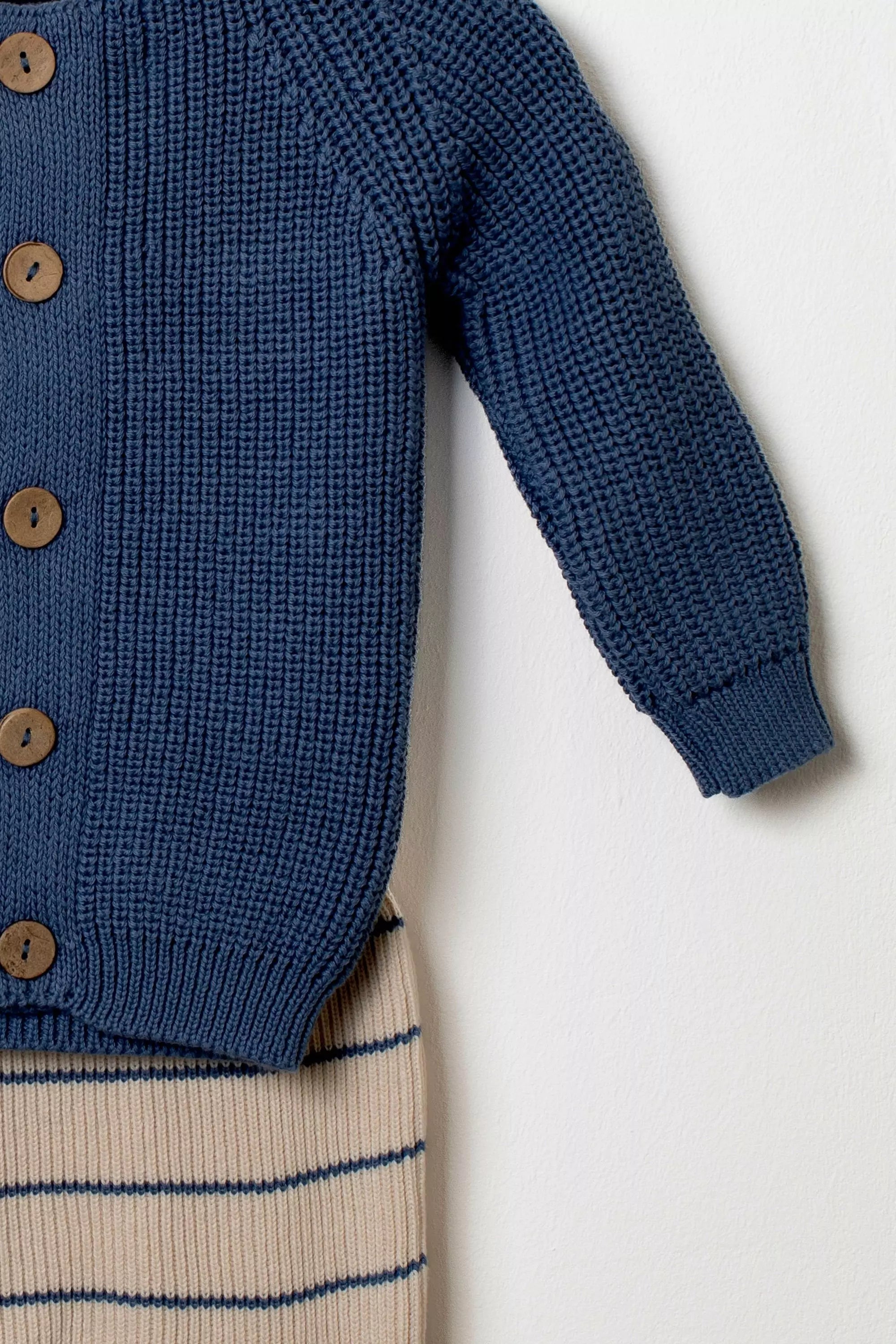 Detailansicht des Ärmels und des Strickmusters des dunkelblauen Baby Cardigans kombiniert mit der gestreiften Strickhose.