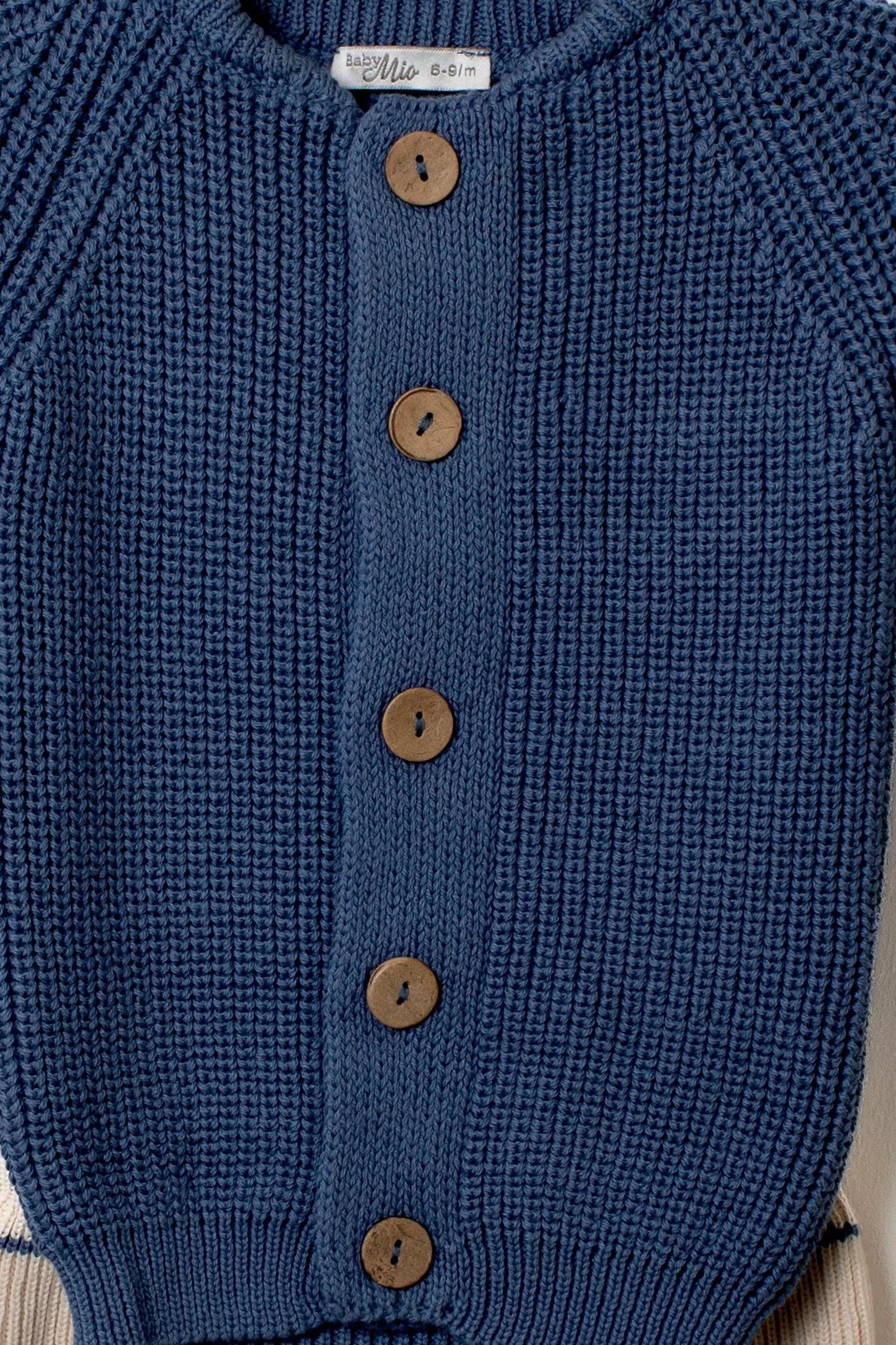 Nahaufnahme der Knopfleiste des marineblauen Baby Strick-Cardigans mit Holzknöpfen und deutlicher Strickstruktur.
