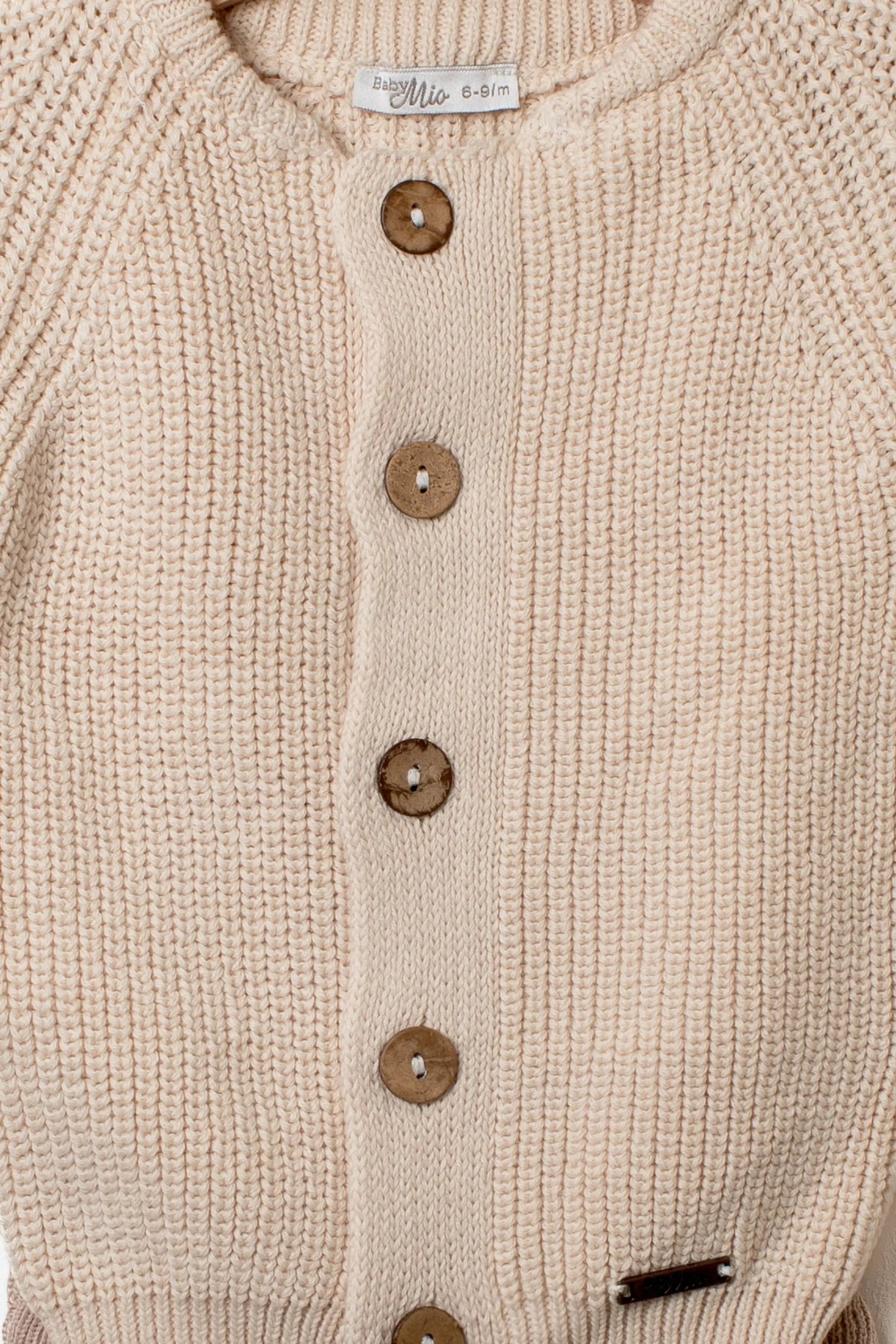 Nahaufnahme der Knopfleiste des beigen Baby Strick-Cardigans mit Holzknöpfen und deutlicher Rippstrick-Struktur.
