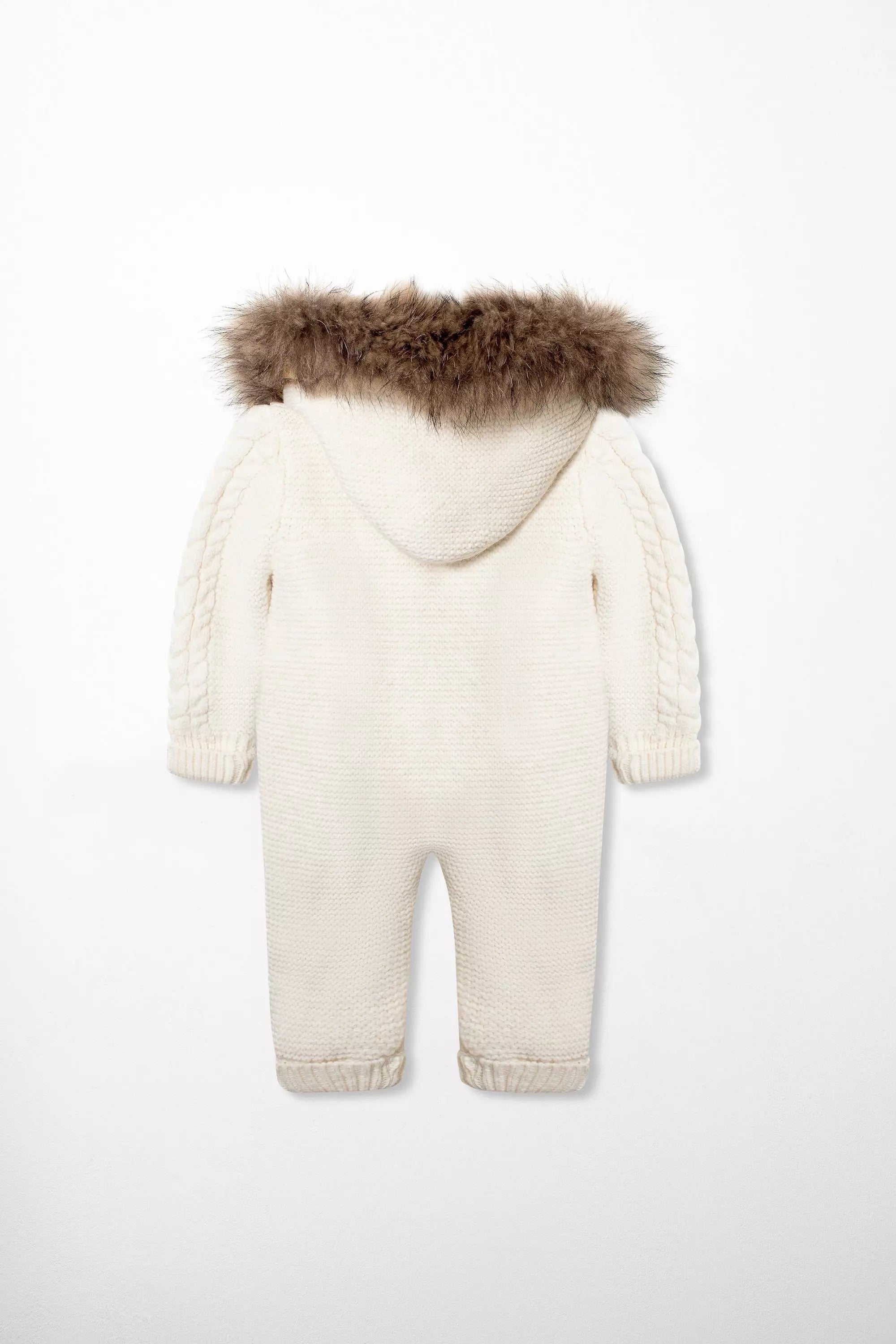 Rückenansicht des Baby-Overalls in Creme-Weiß, mit Kapuze und braunem Pelzbesatz sowie Zopfmuster an den Ärmeln