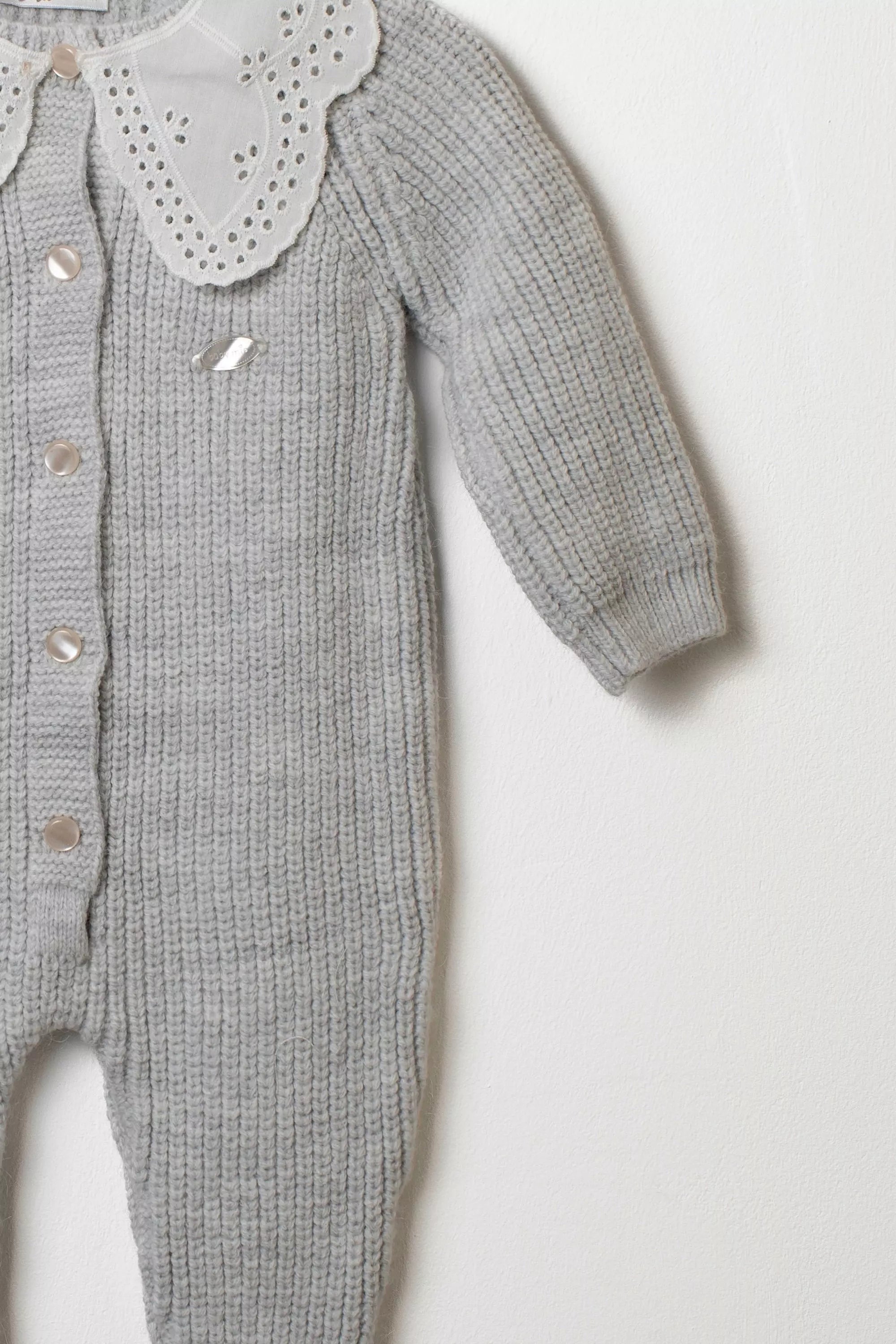 Detailansicht des Ärmels und des Lochstickerei-Kragens des grauen Baby Strick-Overalls.
