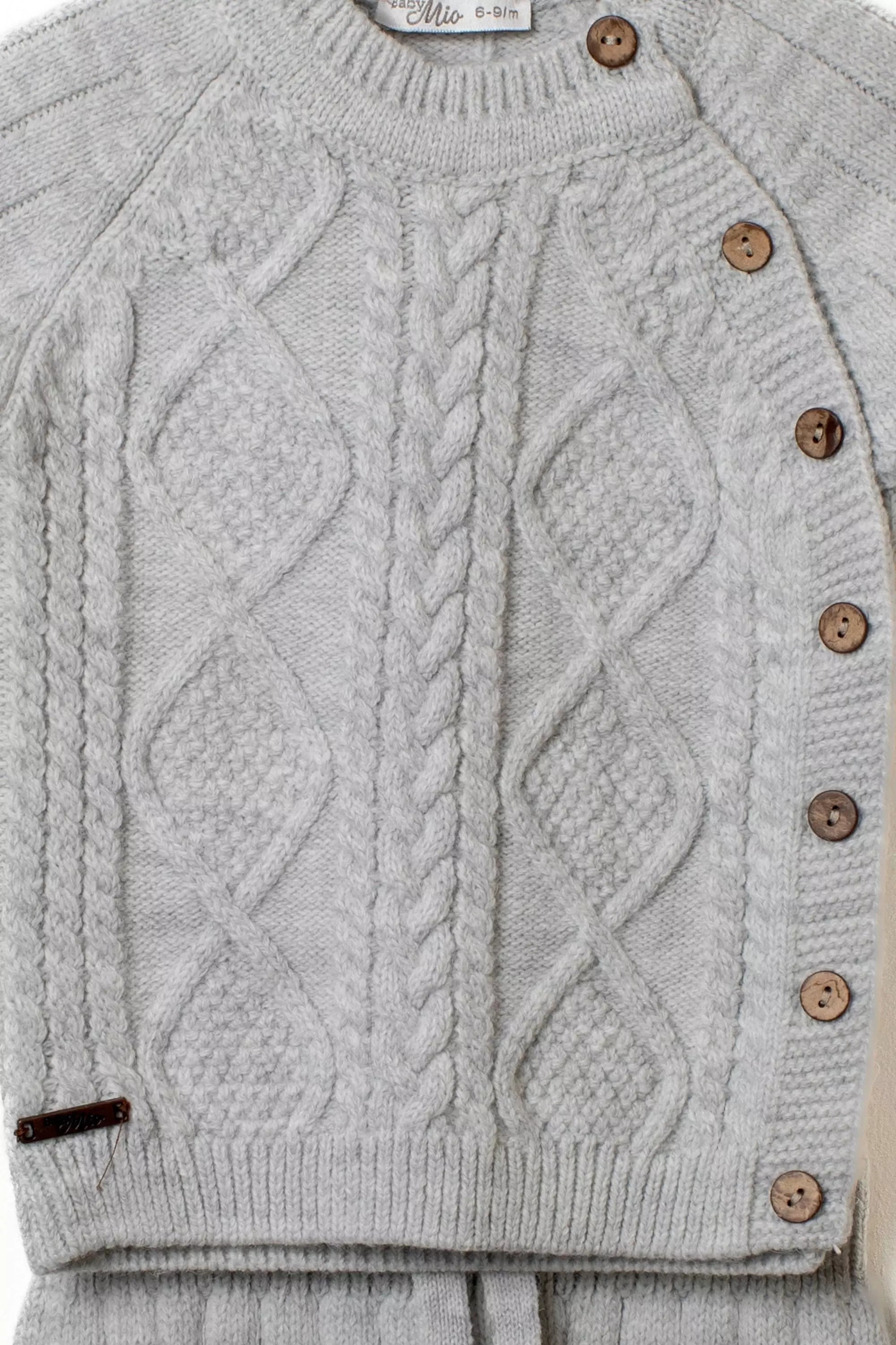 Nahaufnahme des grauen Baby Strickpullovers mit detailliertem Zopf und Rautenmuster sowie Holzknopfleiste an der Schulter