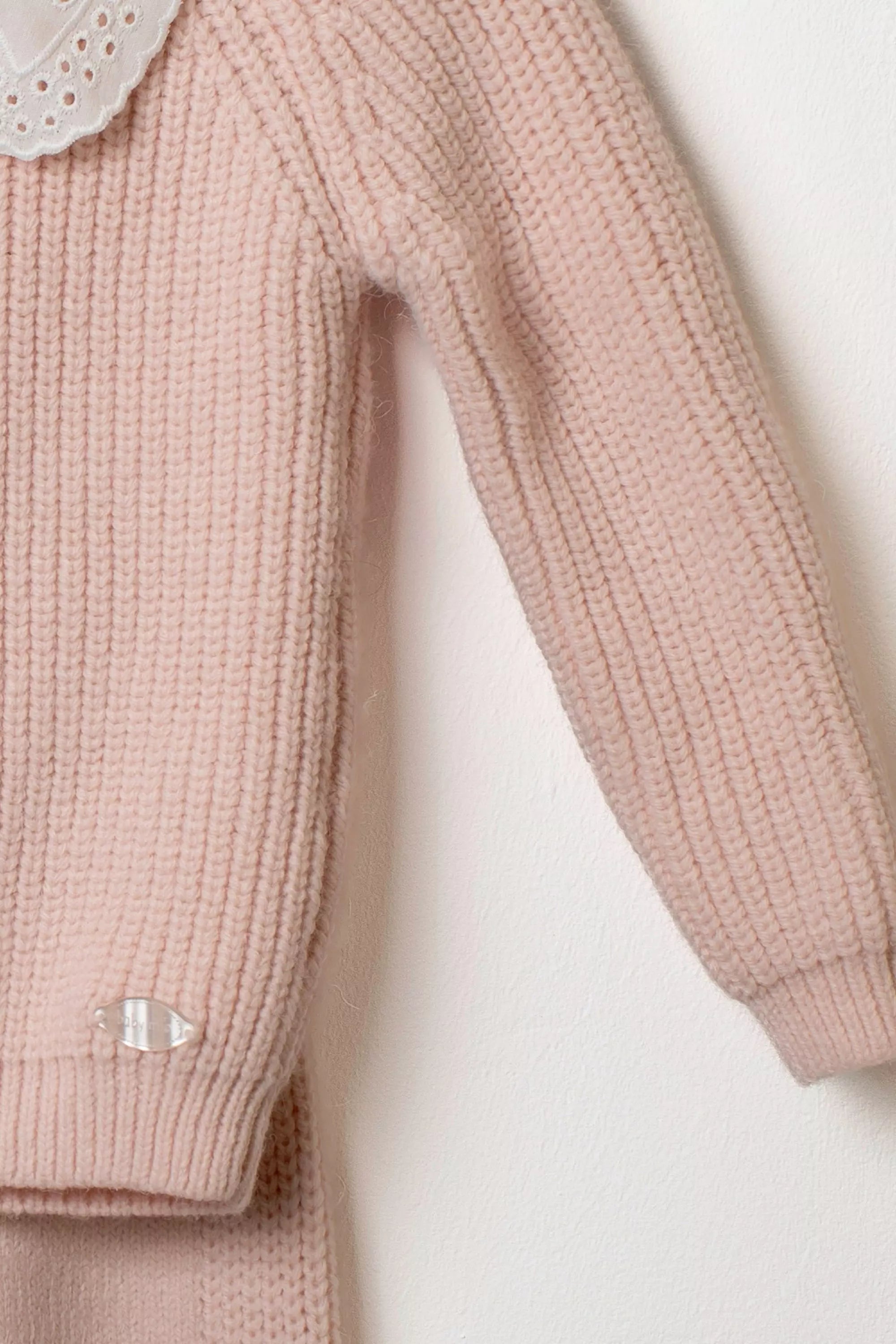 Nahaufnahme des Ärmels des rosa Strickpullovers mit Rippstrickmuster und kleinem Logo Detail