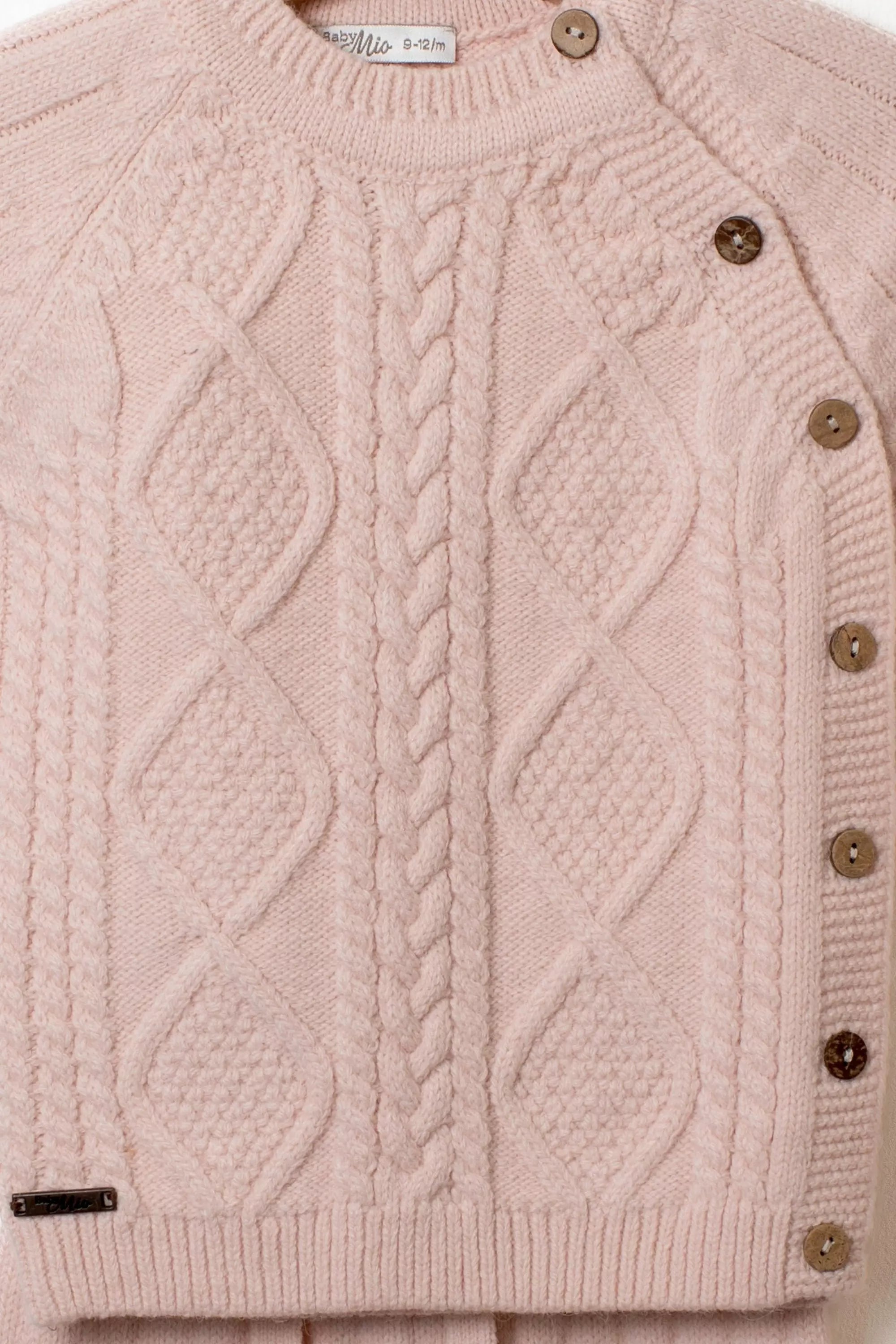 Nahaufnahme des rosa Baby Strickpullovers mit detailliertem Zopf und Rautenmuster sowie Holzknopfleiste an der Schulter