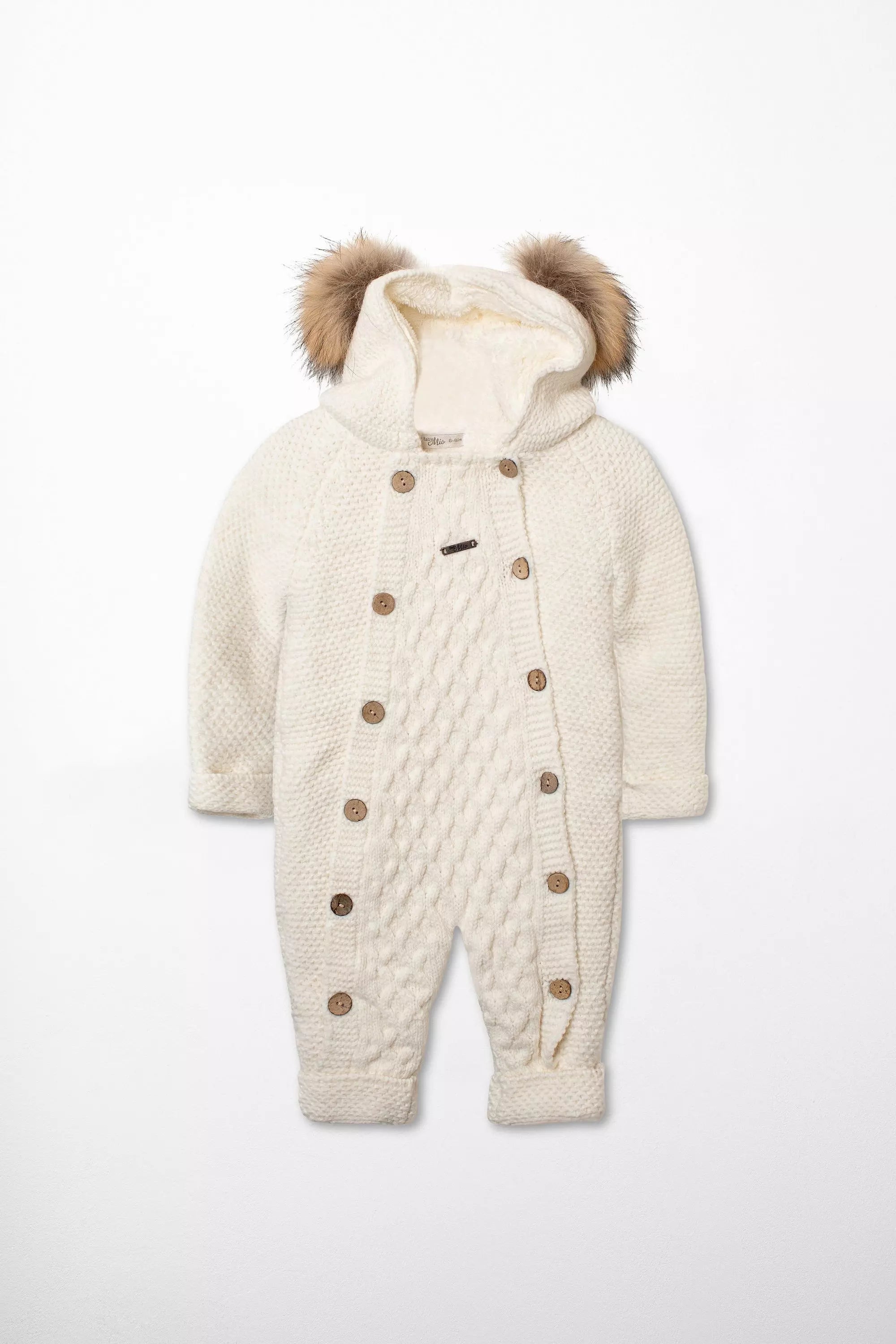 Vorderansicht des warm gefütterten Baby Strick-Schneeanzugs in Weiß mit Zopfmuster, Kapuze mit Webpelz-Ohren und doppelter Knopfleiste.