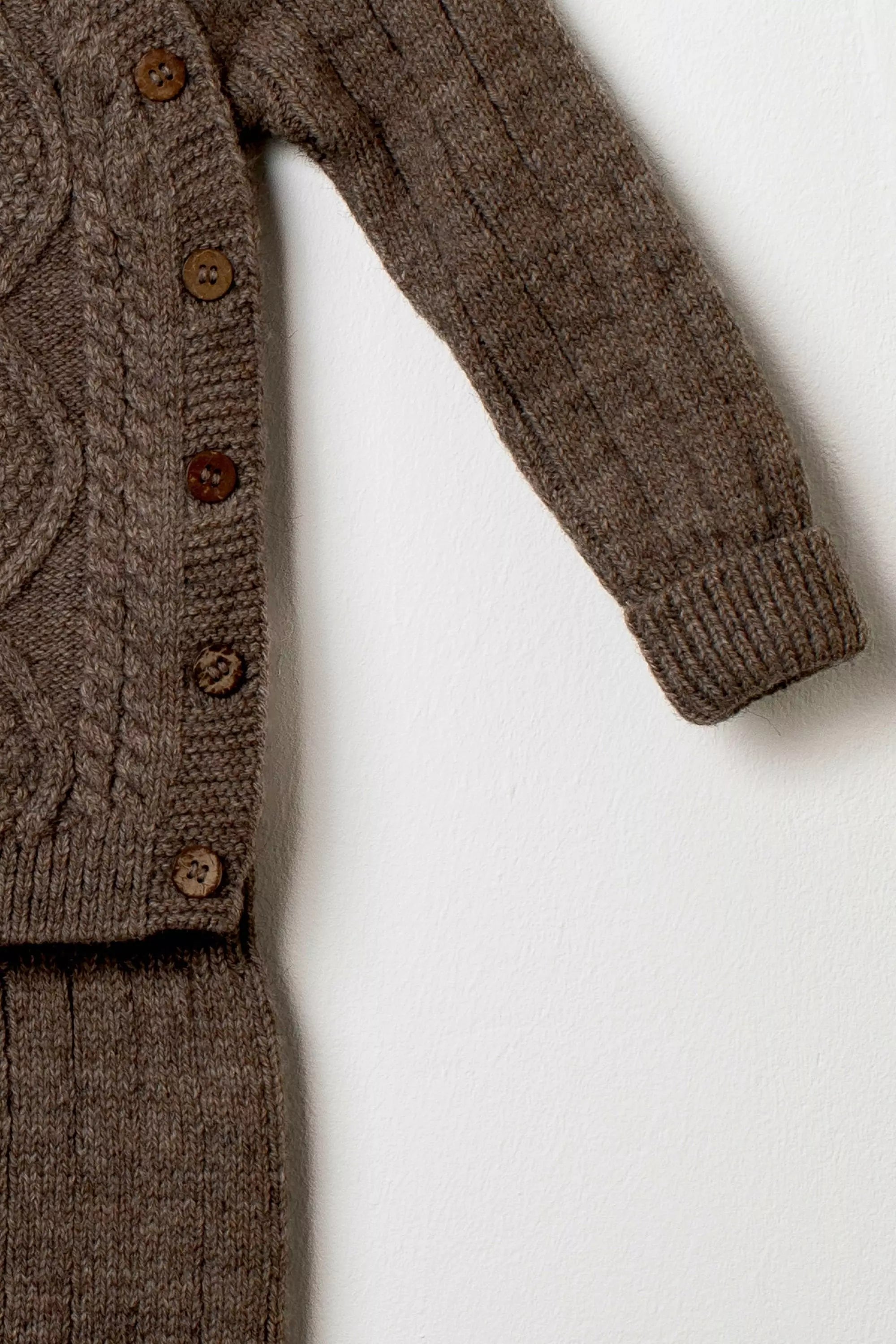 Nahaufnahme des Ärmels des braunen Strickpullovers mit Knopfleiste aus Holzknöpfen und Rippstrick der Hose