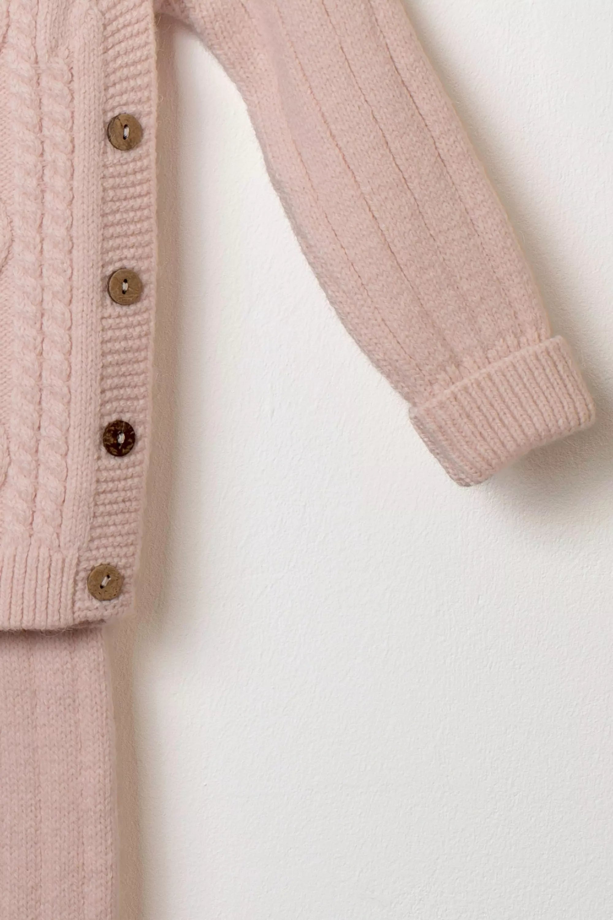 Nahaufnahme des Ärmels des rosa Strickpullovers mit Knopfleiste aus Holzknöpfen und Rippstrick der Hose