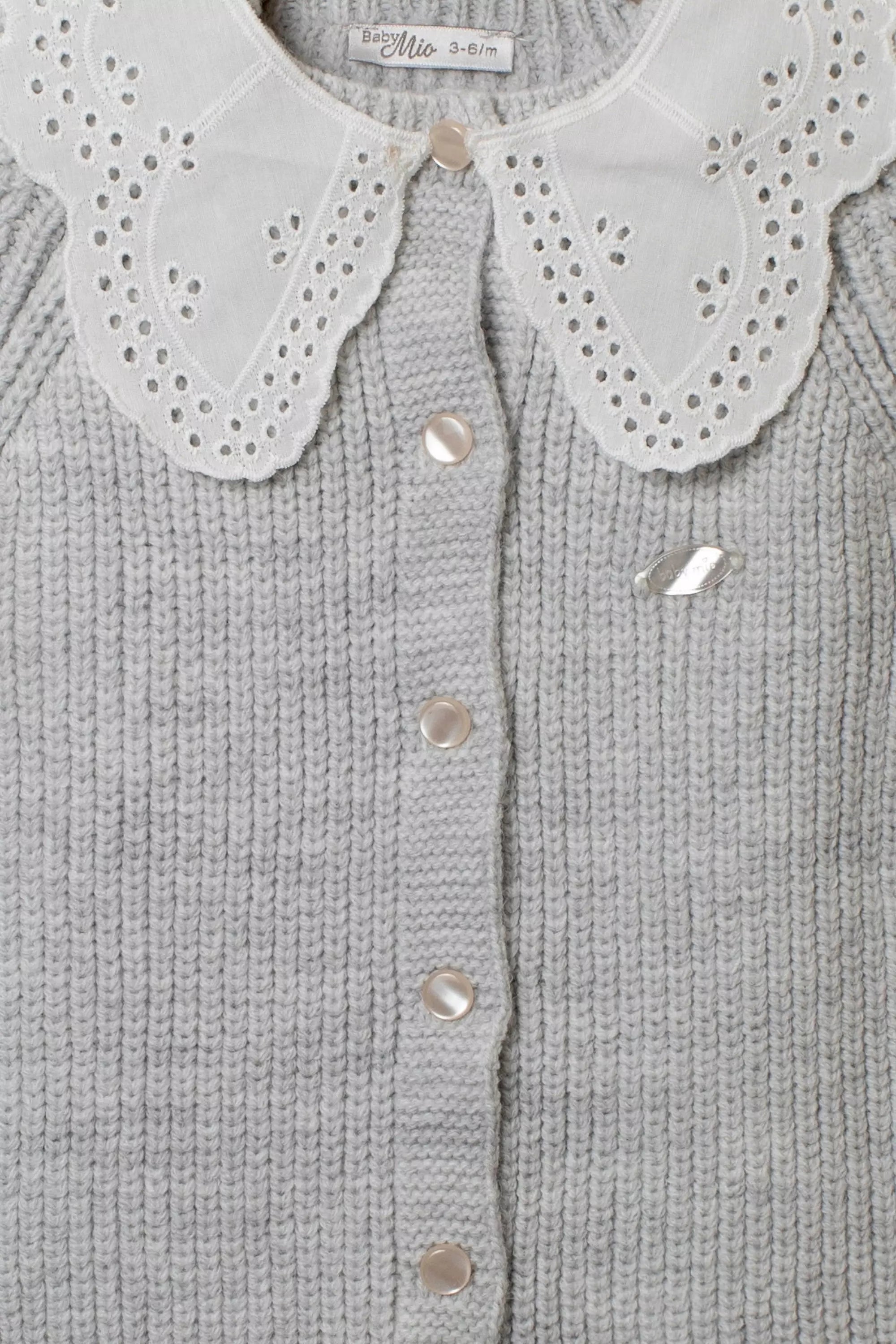 Nahaufnahme des grauen Strick-Stramplers mit weißem Lochstickerei-Kragen und glänzenden Perlmutt-Knöpfen.