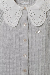 Nahaufnahme des grauen Strick-Stramplers mit weißem Lochstickerei-Kragen und glänzenden Perlmutt-Knöpfen.
