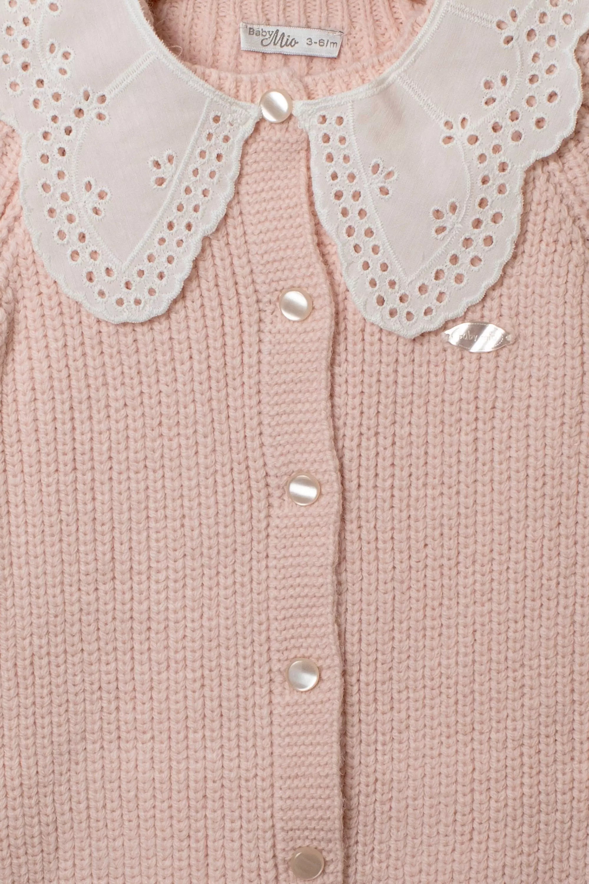 Nahaufnahme des rosa Strick-Stramplers mit weißem Lochstickerei-Kragen und glänzenden Perlmutt-Knöpfen.