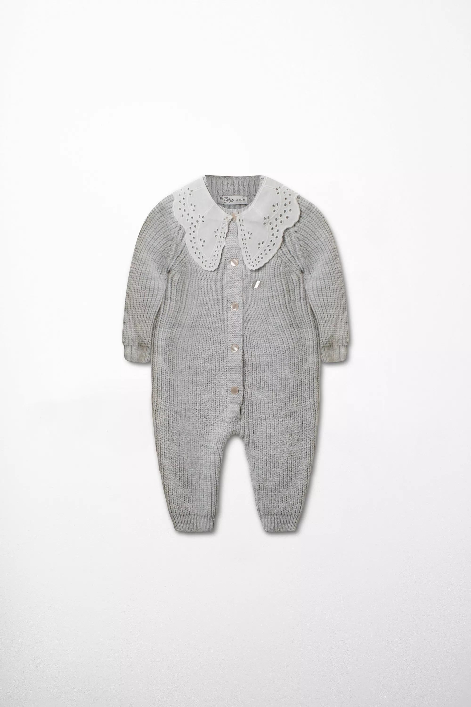 Vorderansicht des Baby Strick-Stramplers in Grau mit großem weißen Kragen mit Lochstickerei und Perlmutt-Knöpfen.