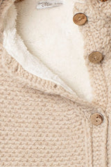 Nahaufnahme des beigen Baby Strickanzugs mit kuscheligem Teddyfutter und rustikalen Holzknöpfen. Detailansicht der hochwertigen Strickstruktur.