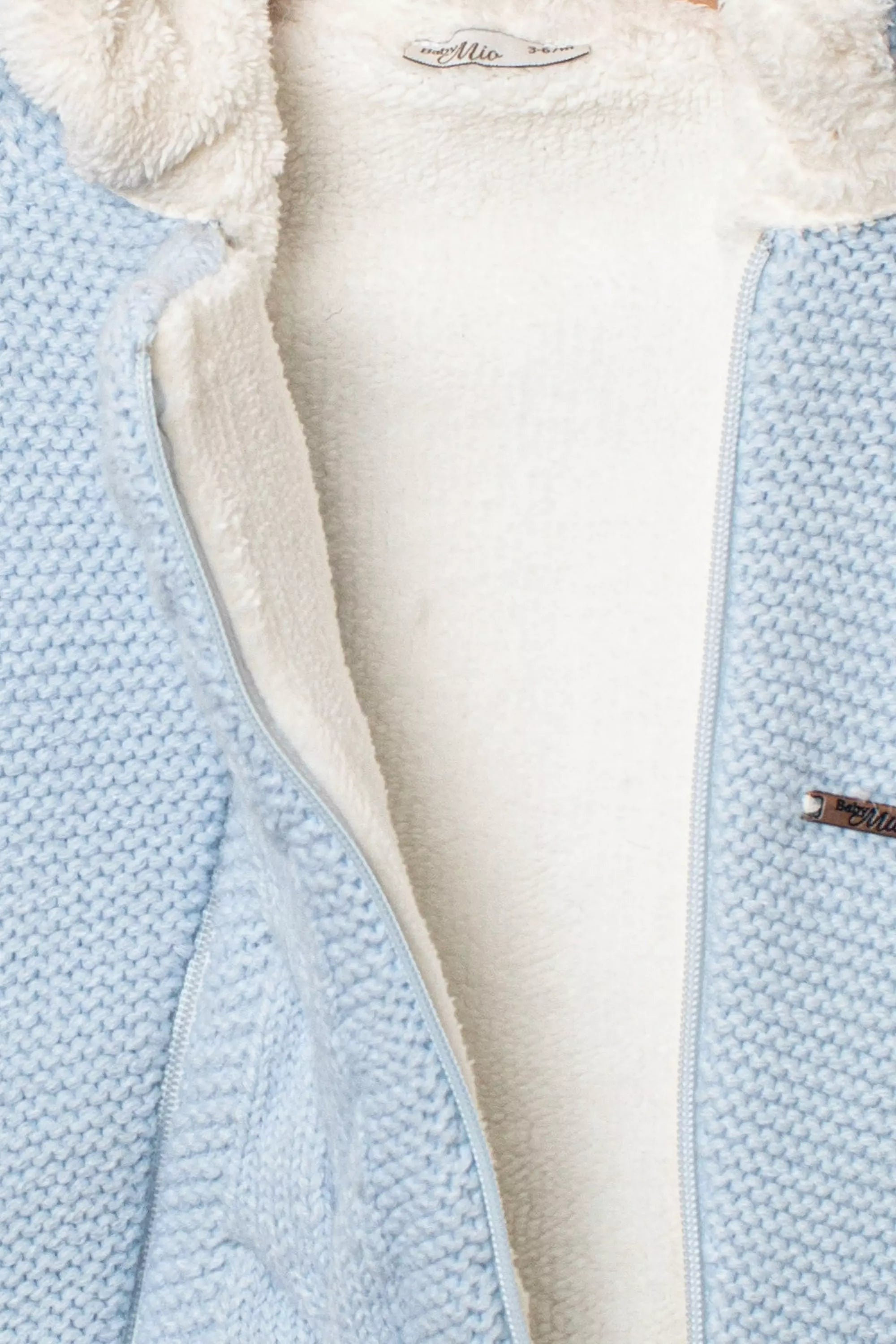Detail des geöffneten Baby Strickstramplers in Hellblau mit weissem kuscheligen Fleecefutter und Reissverschluss