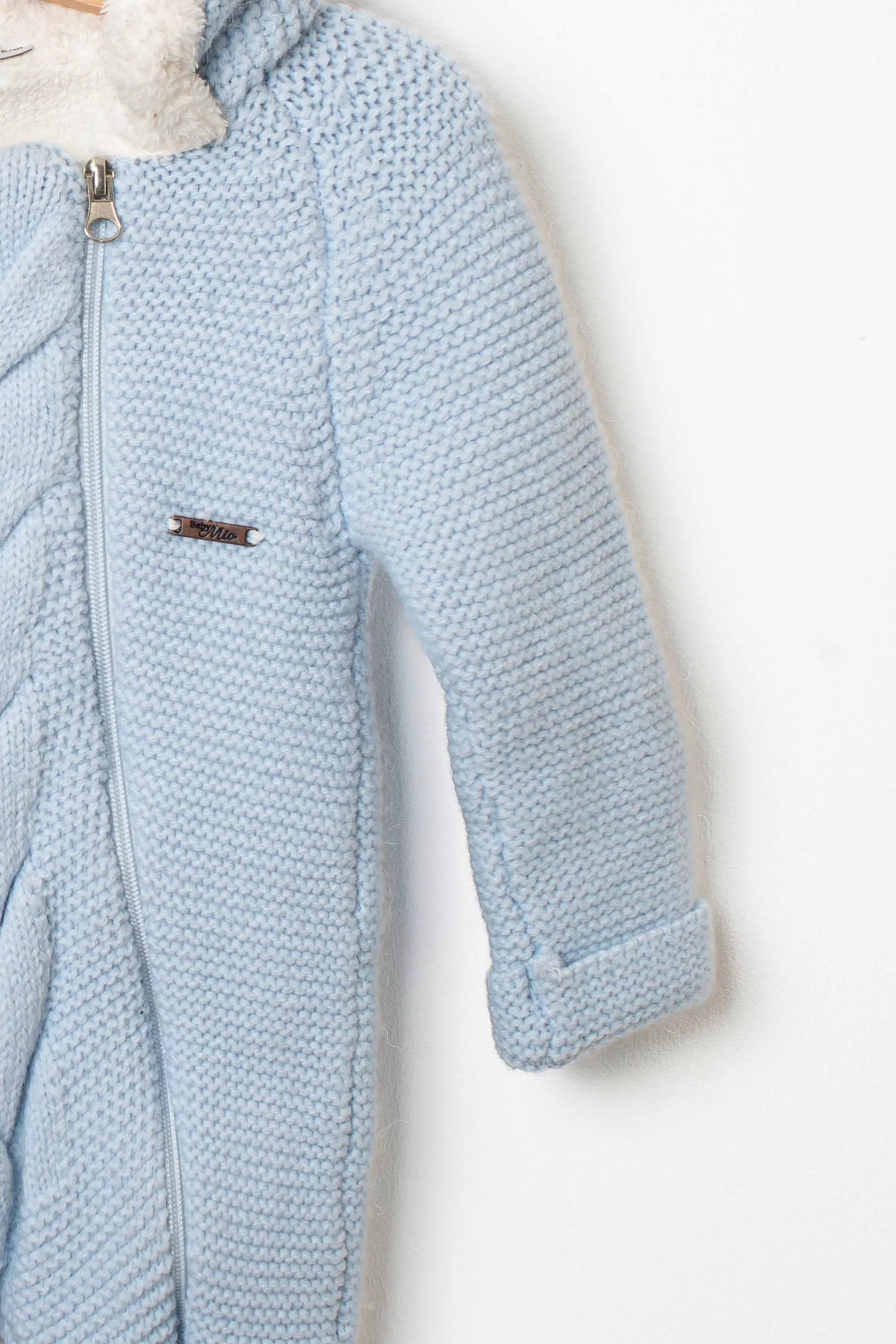 Nahaufnahme des Baby Strickanzugs in Hellblau Detail des Strickmusters am Ärmel und Reissverschluss