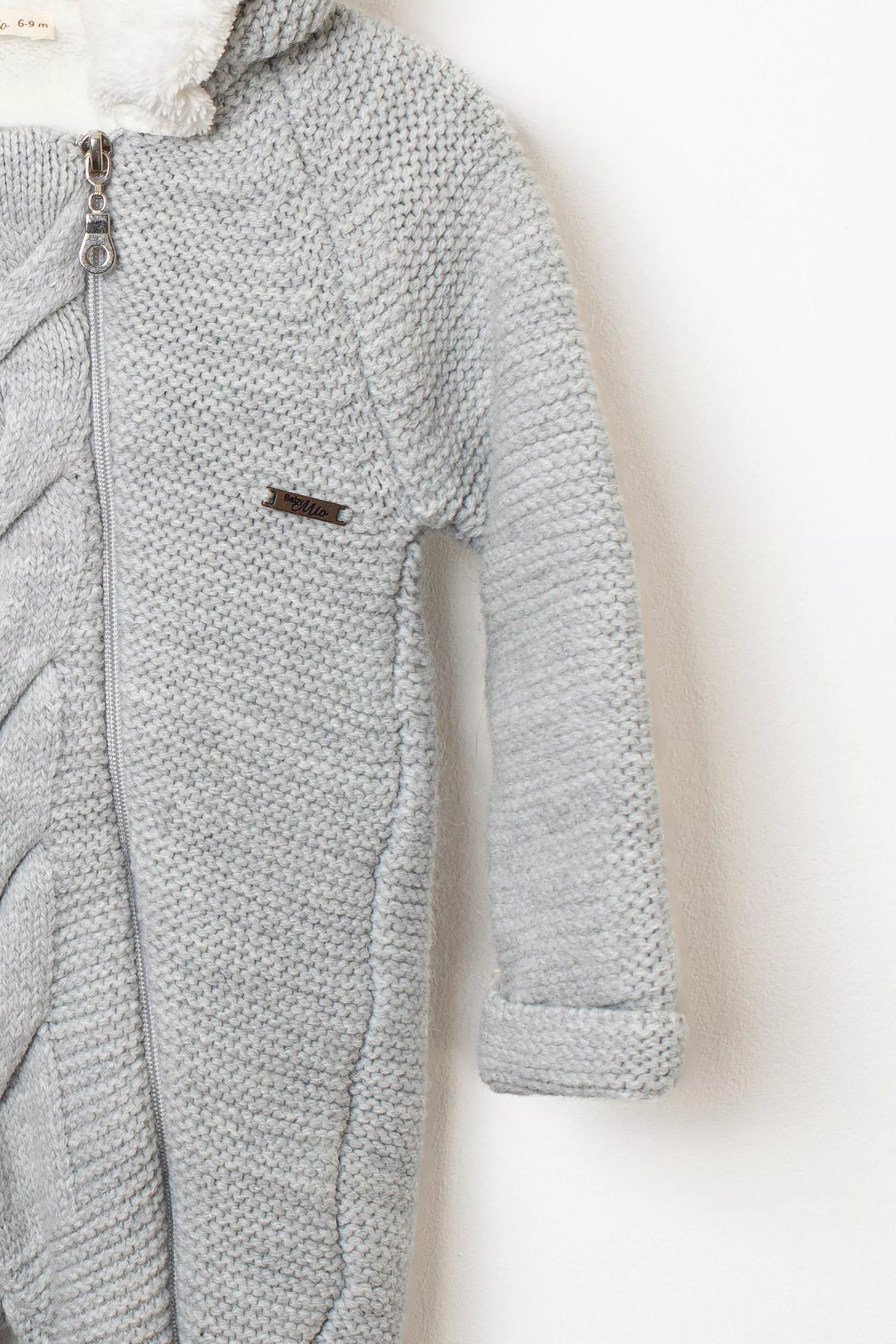 Nahaufnahme des Baby Strickanzugs in Hellgrau Detail des Strickmusters am Ärmel und Reissverschluss