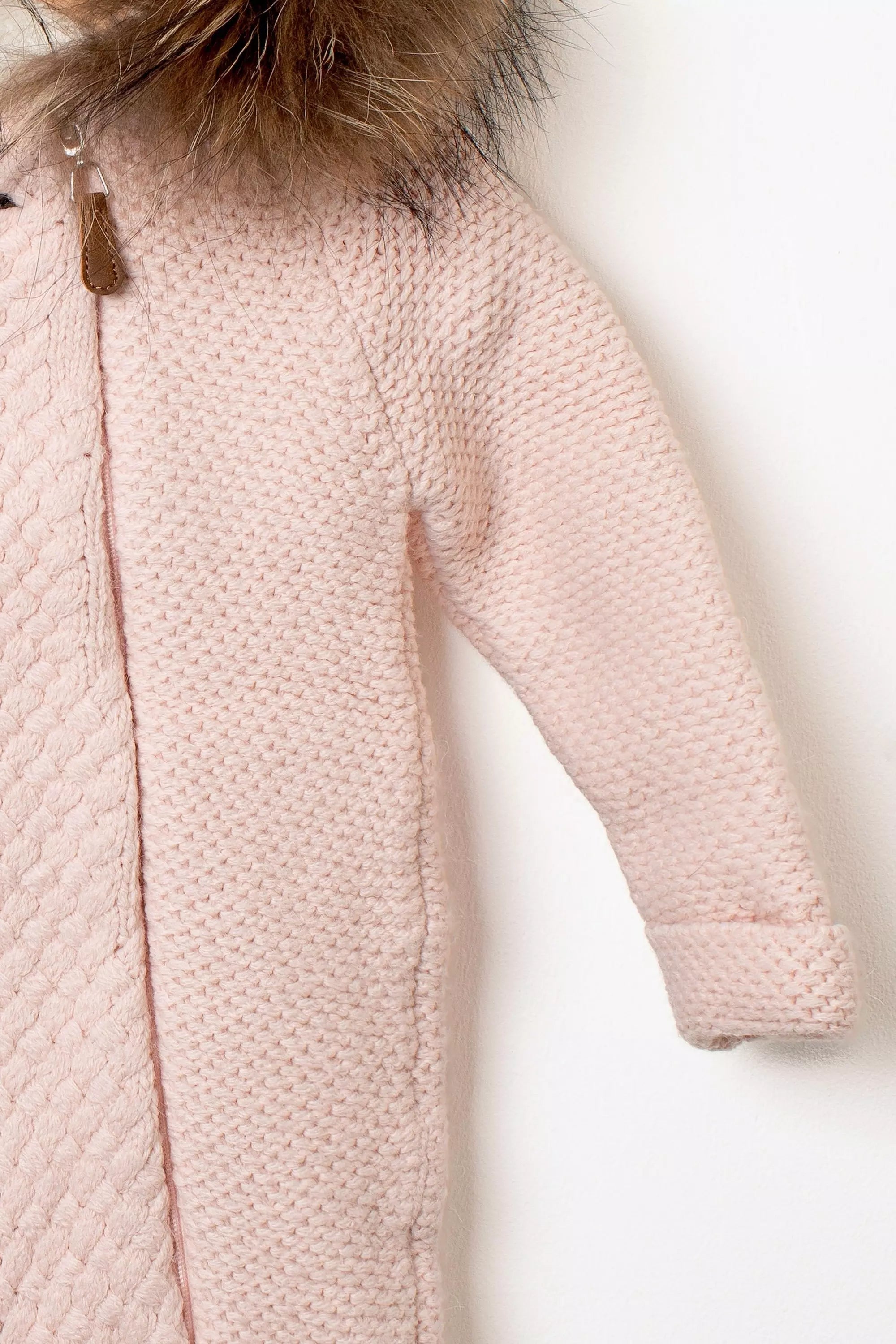 Nahaufnahme des Baby Strickanzugs in Rosa Detail des Strickmusters am Ärmel und Reissverschluss