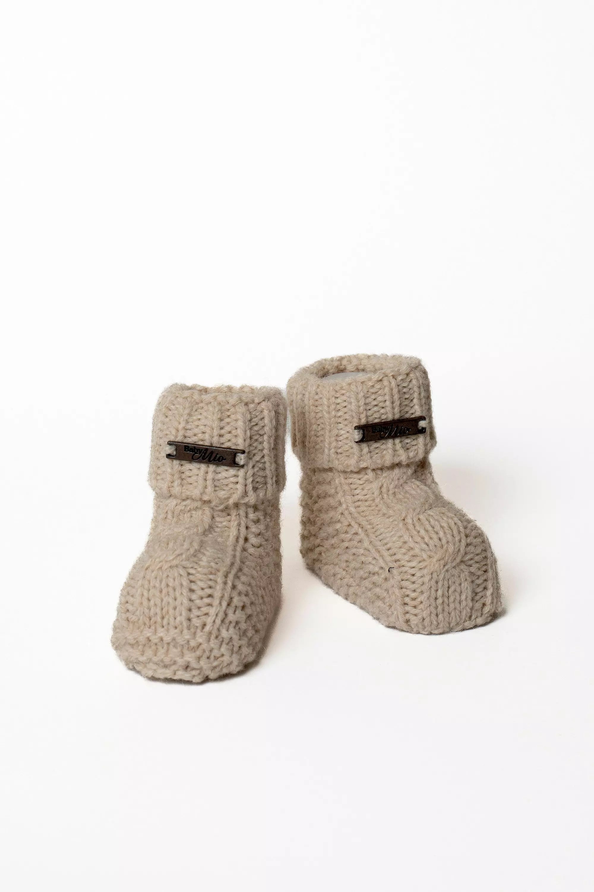 Paar hochwertige beige Baby Strickschuhe mit Zopfmuster und kleinem Label, Warme Strickmode