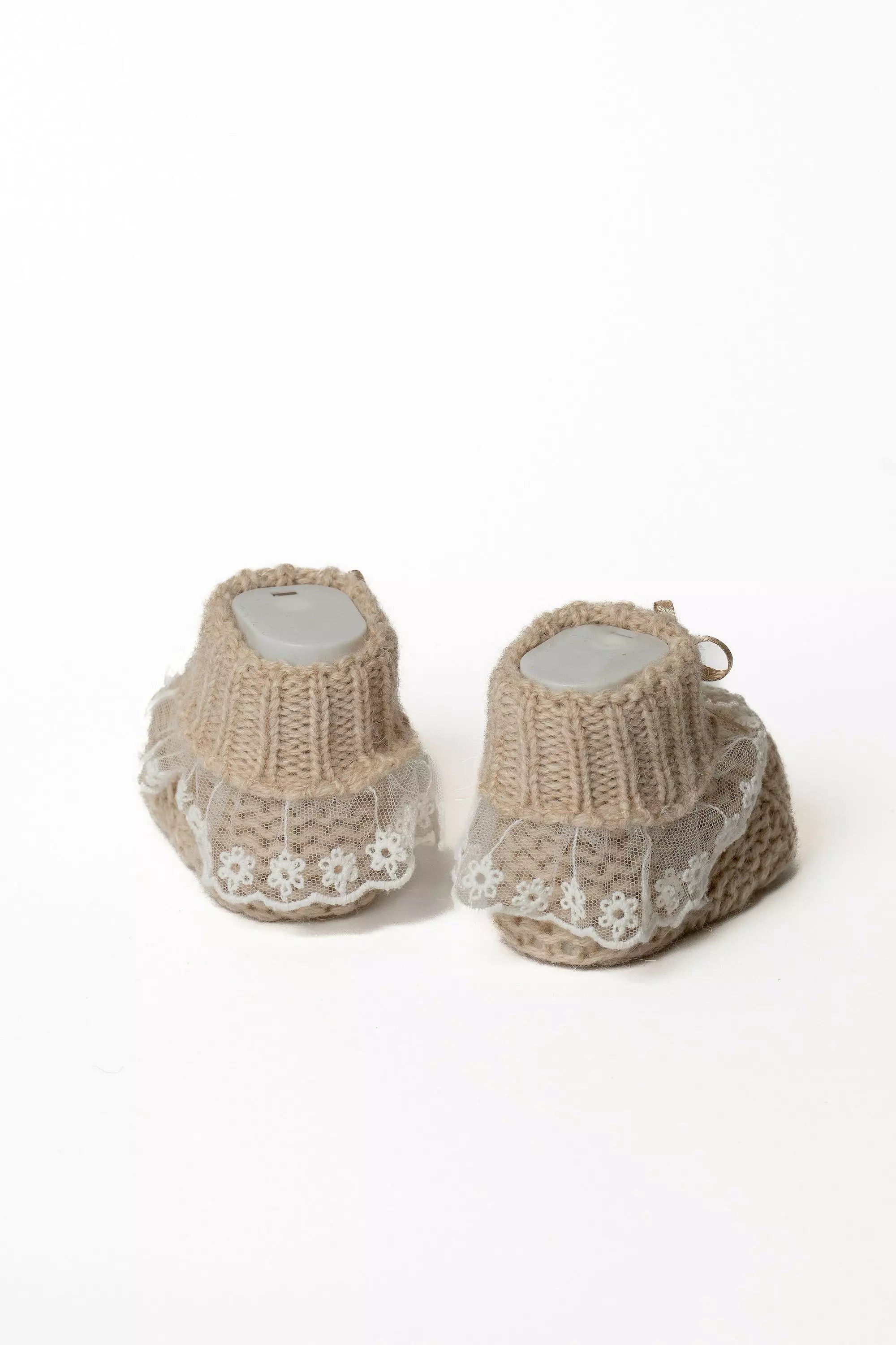 Detailansicht der braunen Babystrickschuhe von hinten, die das breite Rippbündchen und die Spitzenverzierung zeigt.