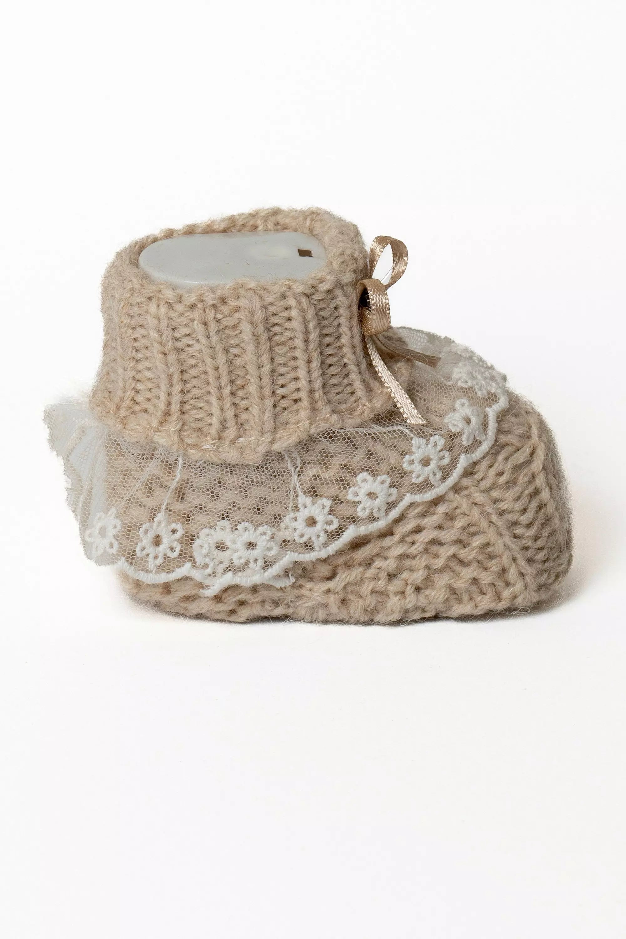 Einzelner beigefarbener Babystrickschuh mit Rippbündchen, weißer Spitzeneinfassung und kleiner beiger Schleife.