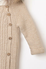 Detailansicht des Ärmels und der Knopfleiste eines beigefarbenen Baby-Strickoveralls mit Zopfmuster und braunen Holzknöpfen