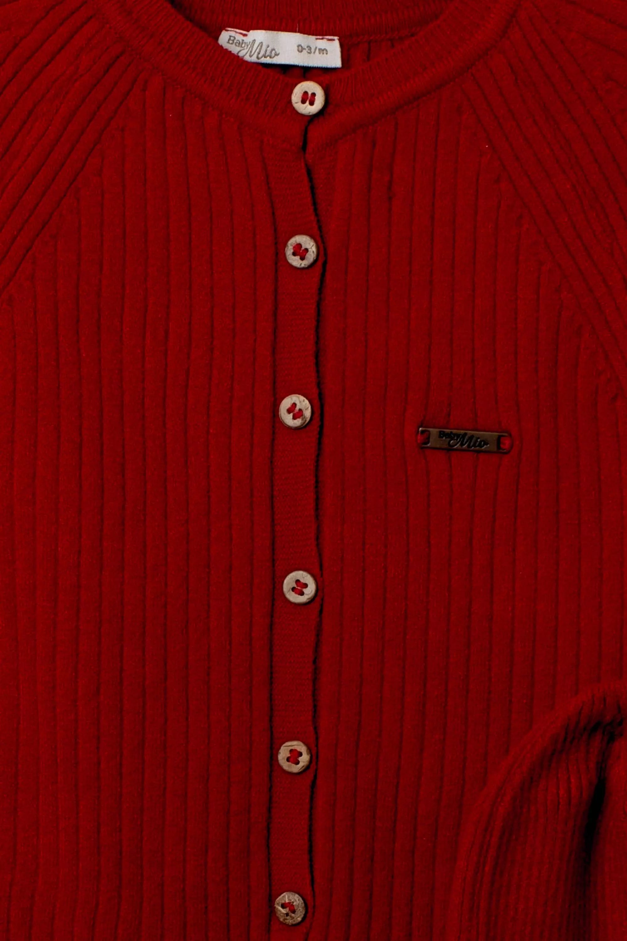 Nahaufnahme der Knopfleiste des roten Baby-Overalls mit Holzeffekt-Knöpfen und Logo-Emblem