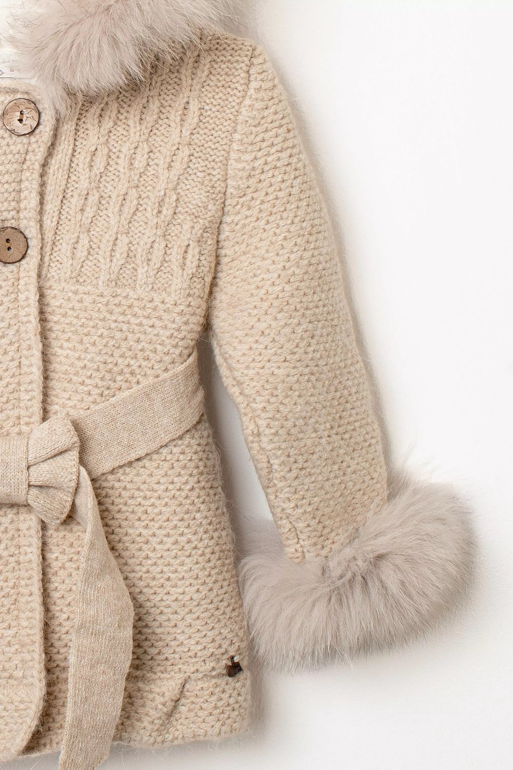 Nahaufnahme Ärmel des beigen Babymantels: Zopfmuster, Strickärmel und Fellmanschetten in Natur