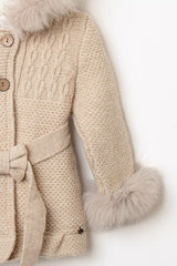 Nahaufnahme Ärmel des beigen Babymantels: Zopfmuster, Strickärmel und Fellmanschetten in Natur