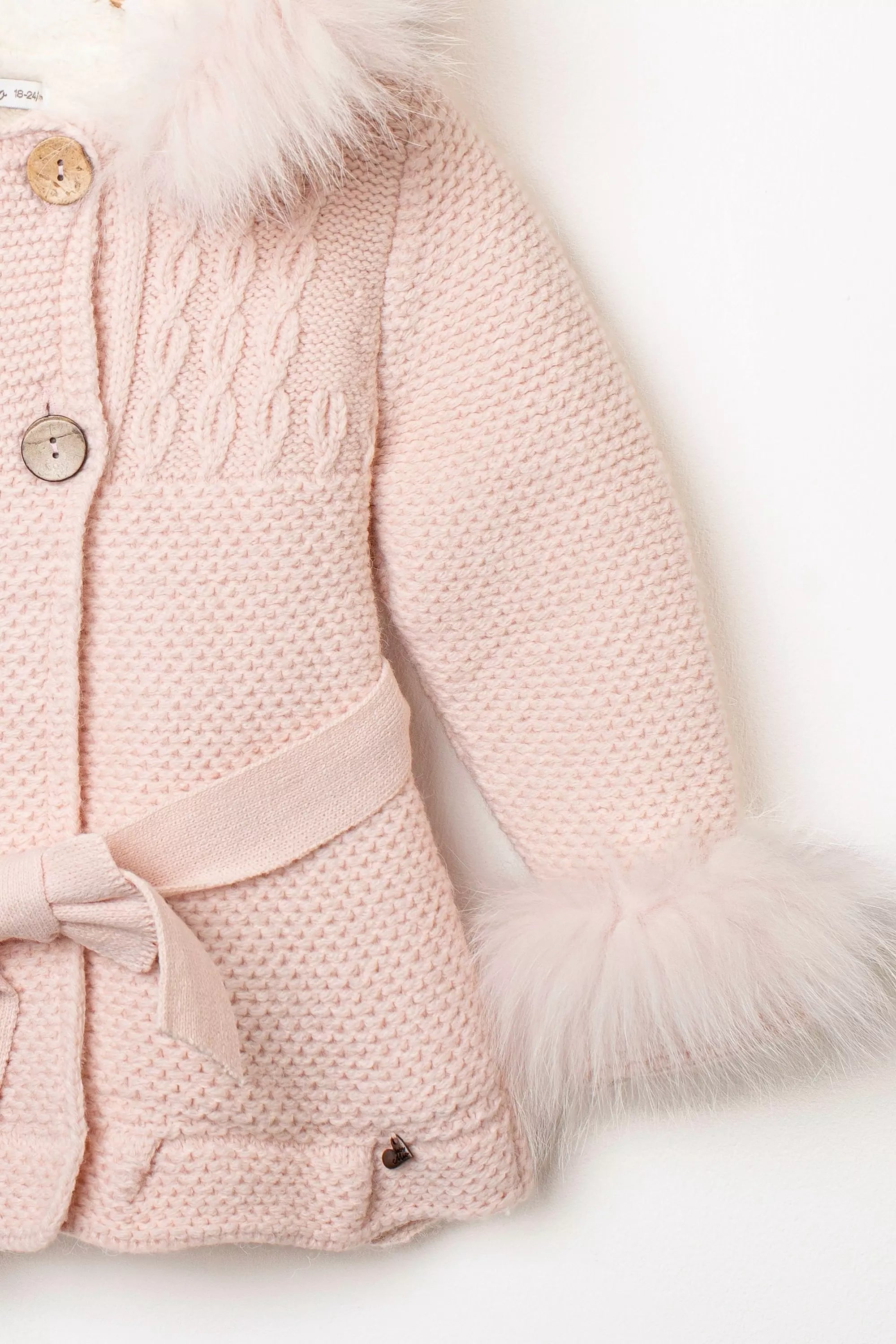 Nahaufnahme Ärmel des rosa Babymantels: Zopfmuster und flauschige Fellmanschetten in Hellrosa