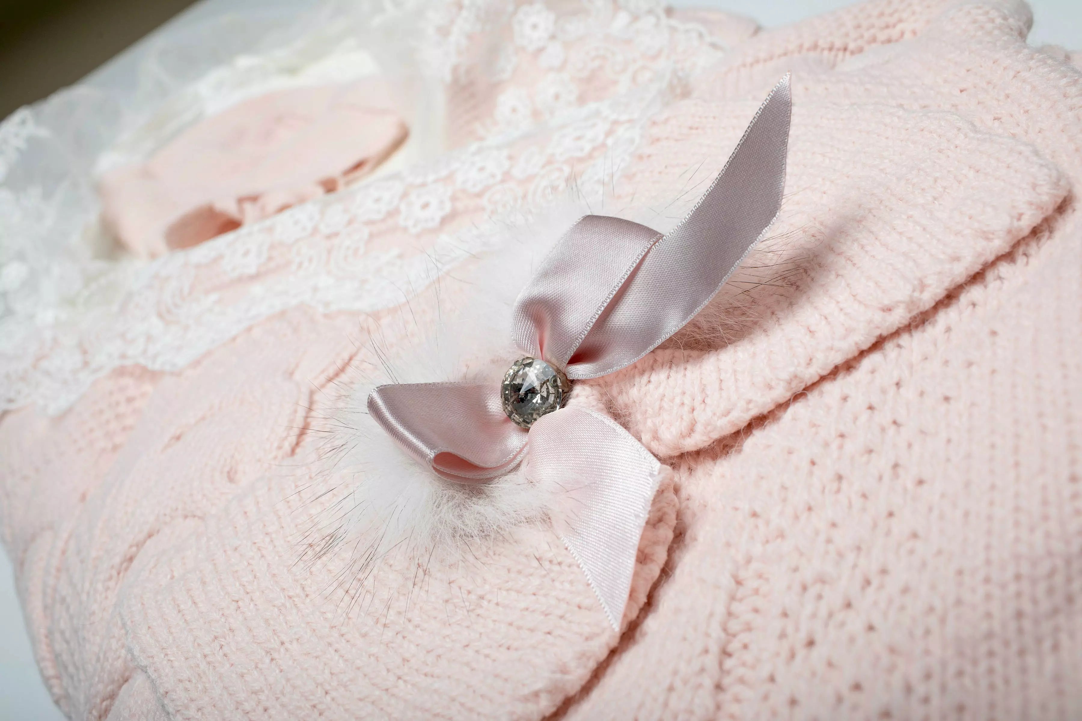 Nahaufnahme der dekorativen rosa Satinschleife mit Strassstein auf dem gestrickten Baby Schlafsack