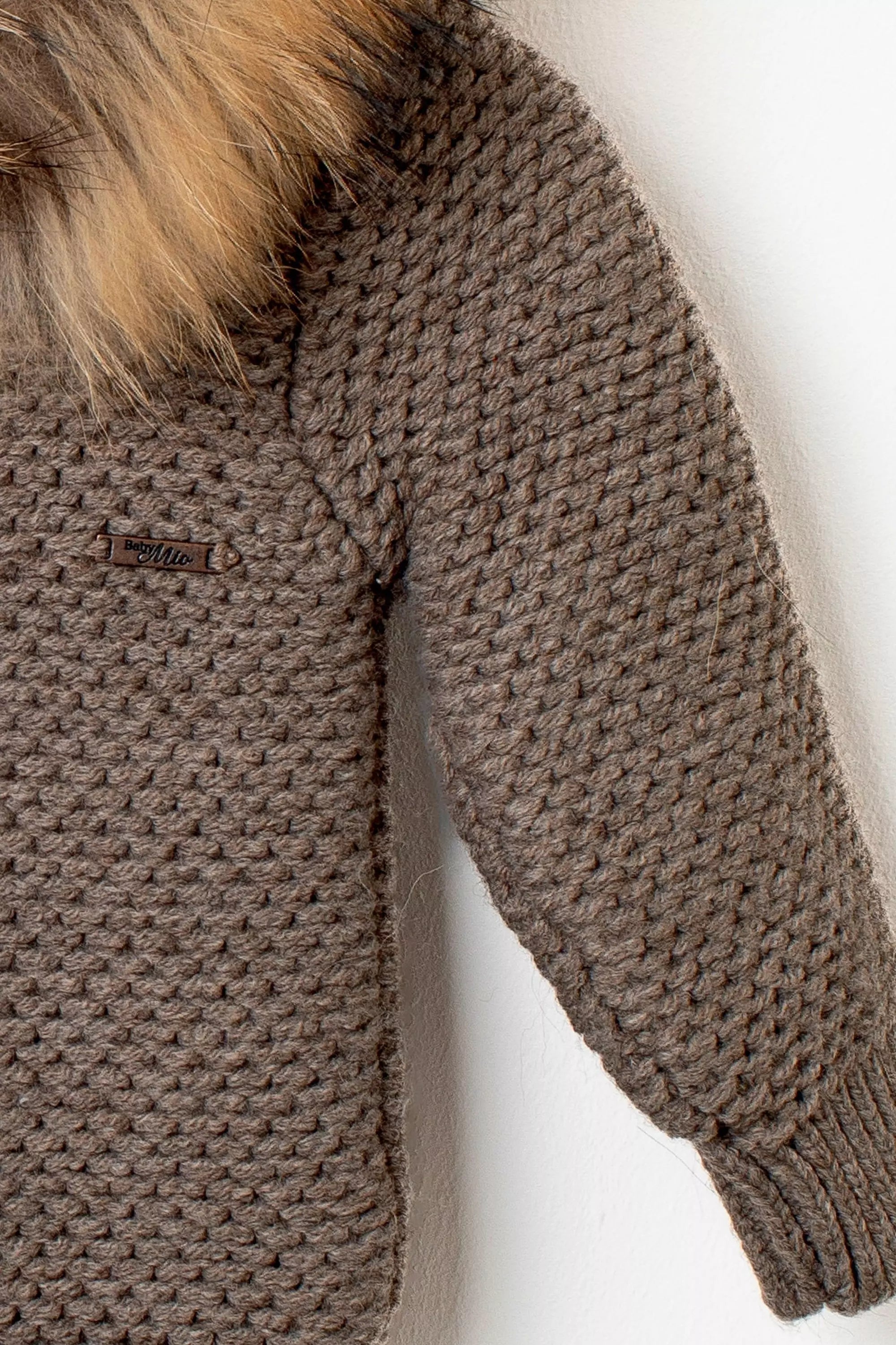 Nahaufnahme der Baby Strickjacke in Braun: Detail des Strickmusters am Ärmel und Logo-Emblem