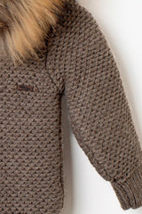 Nahaufnahme der Baby Strickjacke in Braun: Detail des Strickmusters am Ärmel und Logo-Emblem