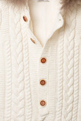 Nahaufnahme der Knopfleiste des creme-weißen Baby-Overalls, mit Zopfmuster und braunen Holzknöpfen auf flauschigem Innenfutter