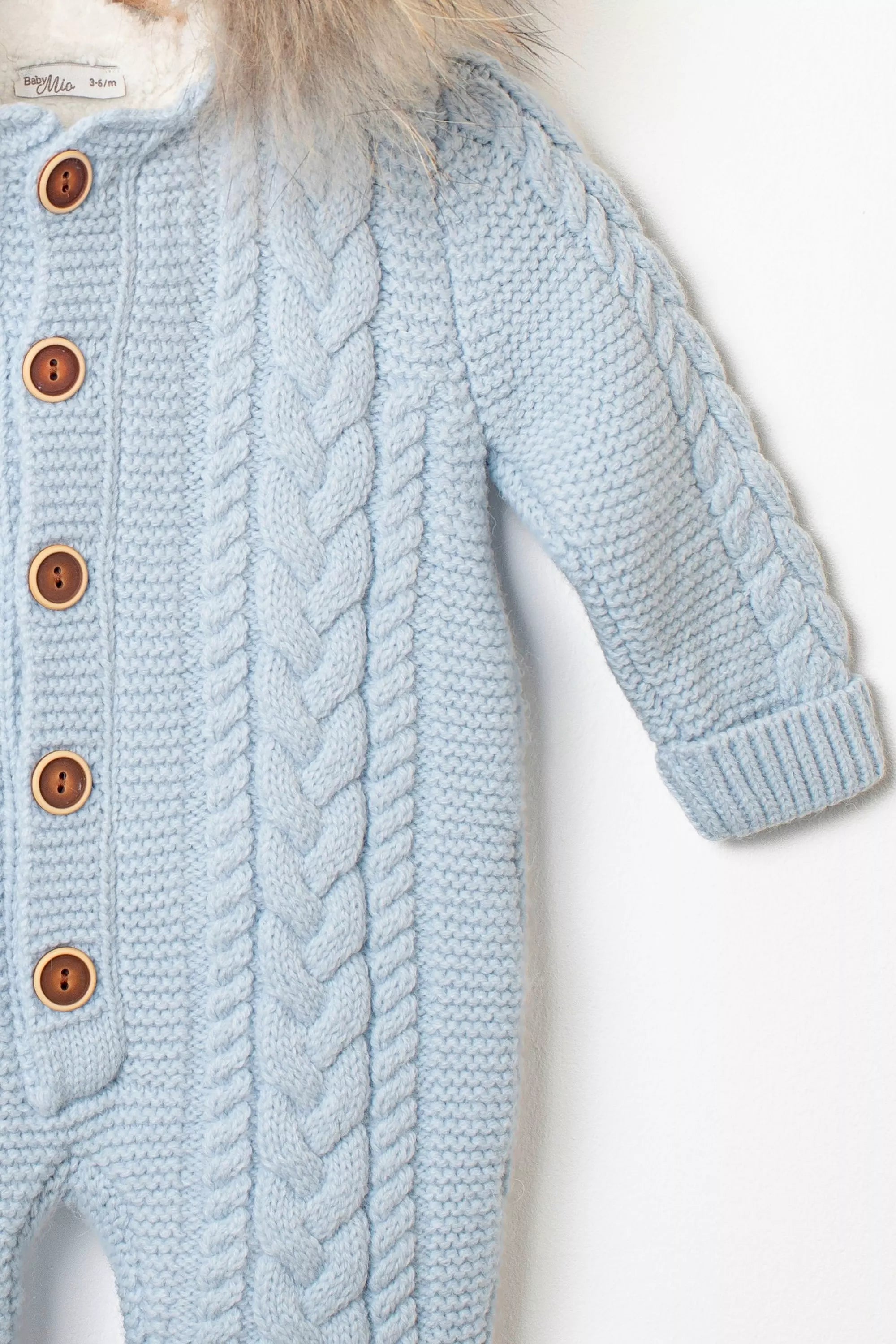 Nahaufnahme des Ärmels des hellblauen Baby-Overalls, mit Zopfmuster und Knopfleiste