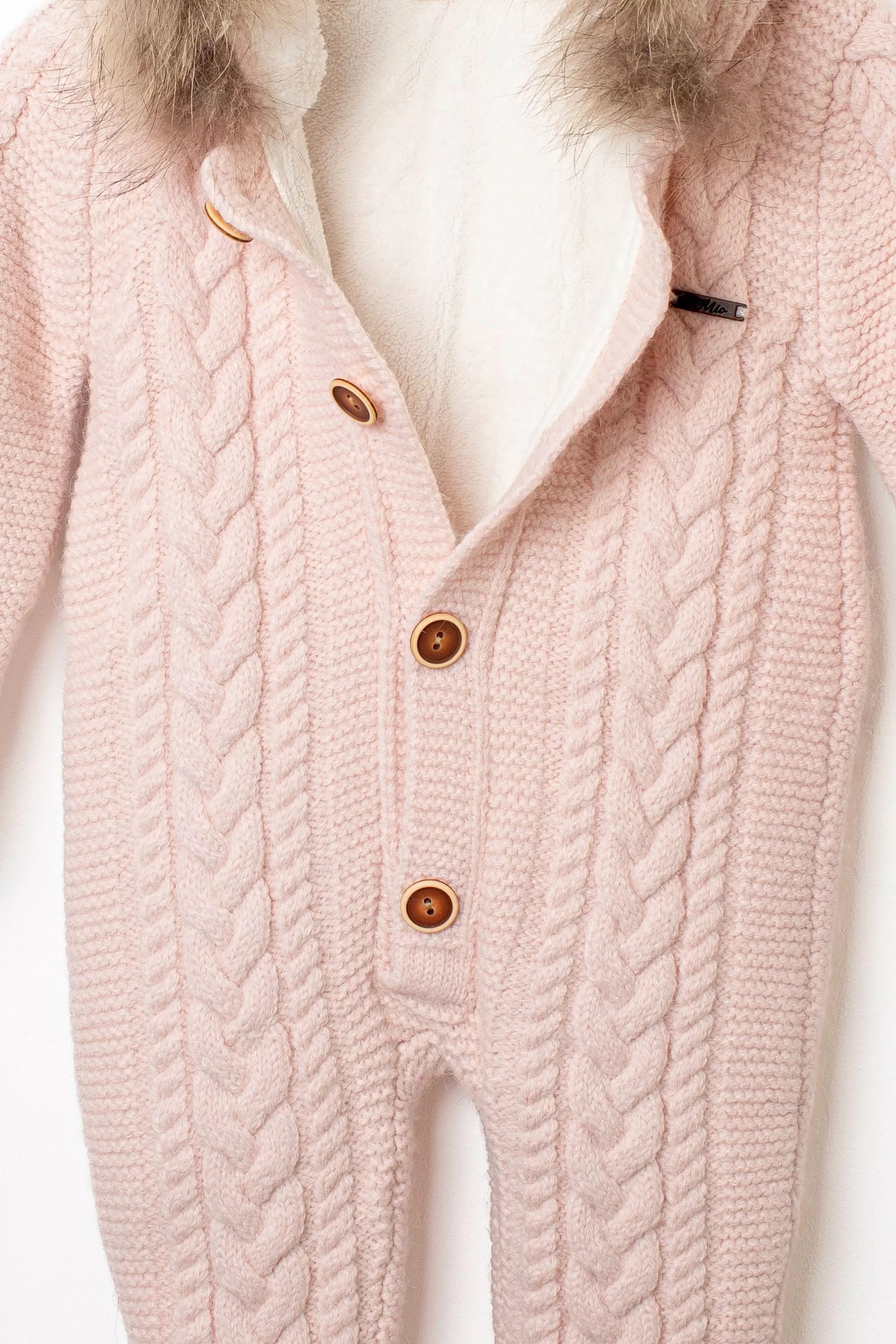 Nahaufnahme der Knopfleiste des rosa Baby-Overalls, mit Zopfmuster, Holzknöpfen und hellem, flauschigem Innenfutter