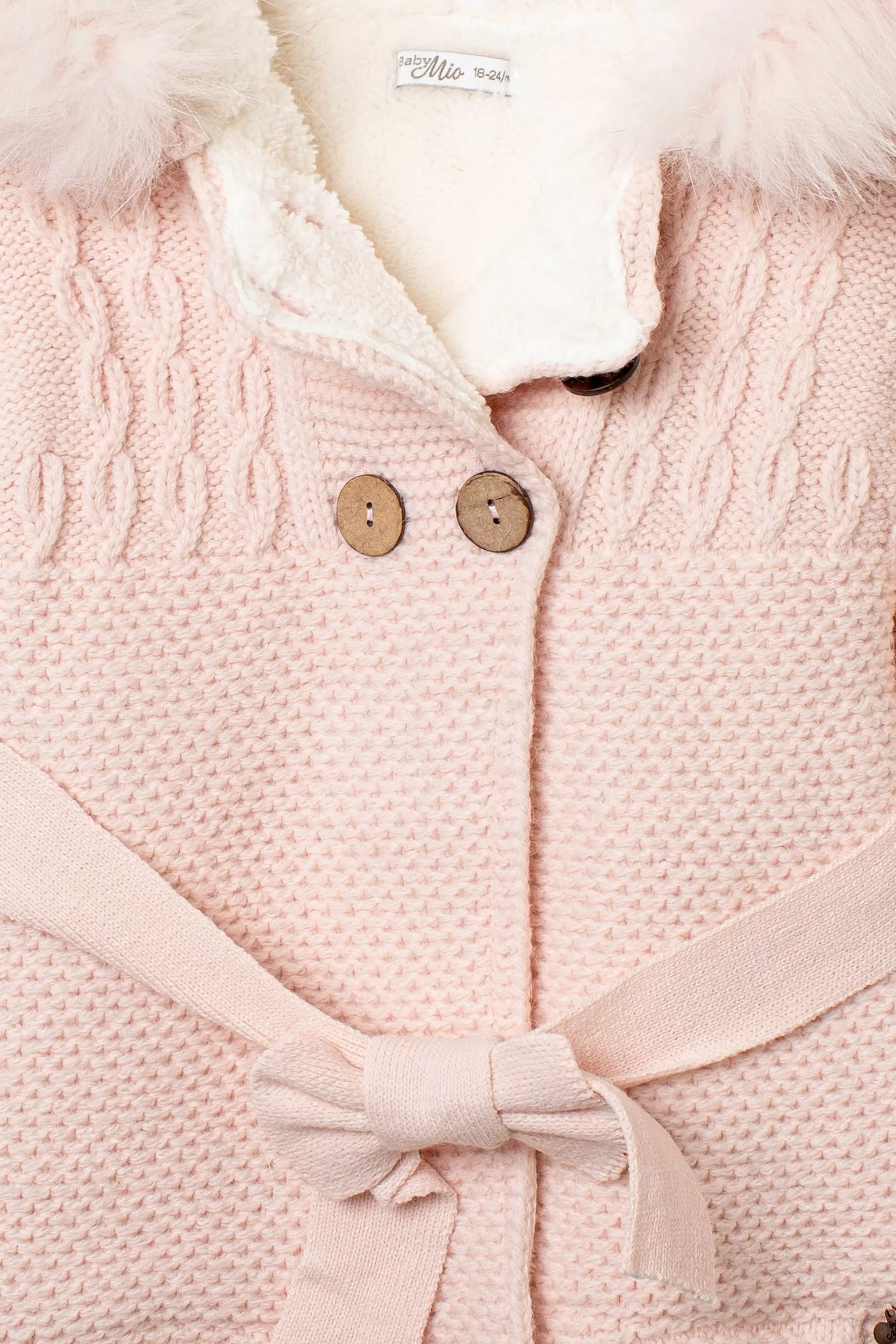 Nahaufnahme Vorderseite des rosa Babymantels: Strick-Zopfmuster, Holzknöpfe und gebundener Gürtel