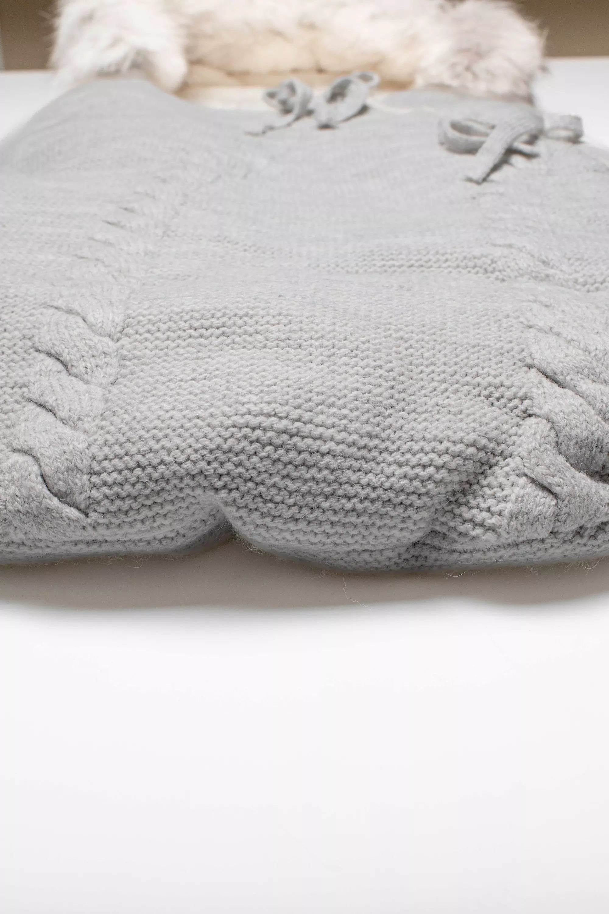 Detailaufnahme der gestrickten Zopfmuster-Struktur an der Unterseite des Baby-Schlafsacks in Grau