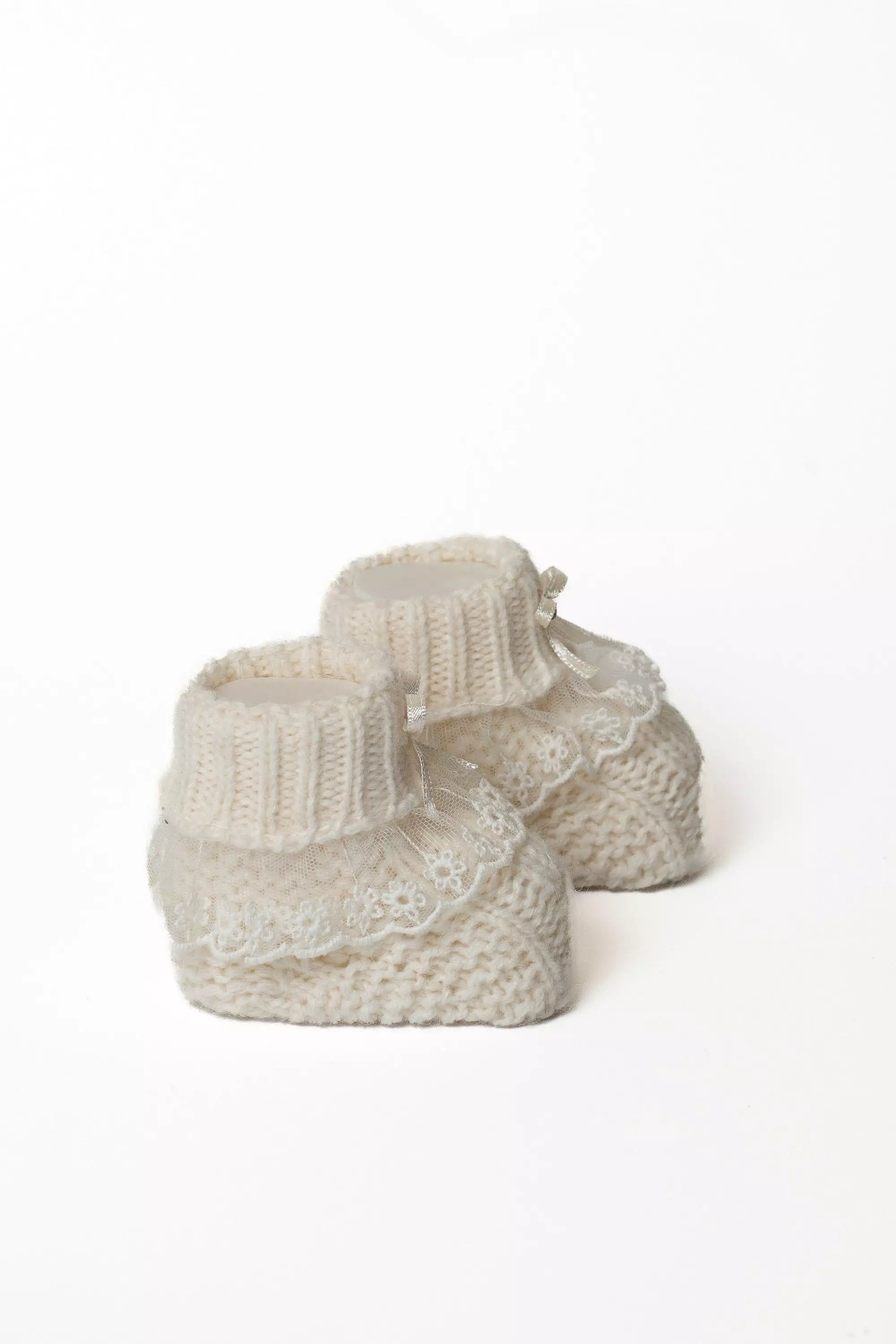 Detailansicht von zwei weißen Babystrickschuhen, die das Rippbündchen und die Rüschen aus feiner Spitze zeigen.