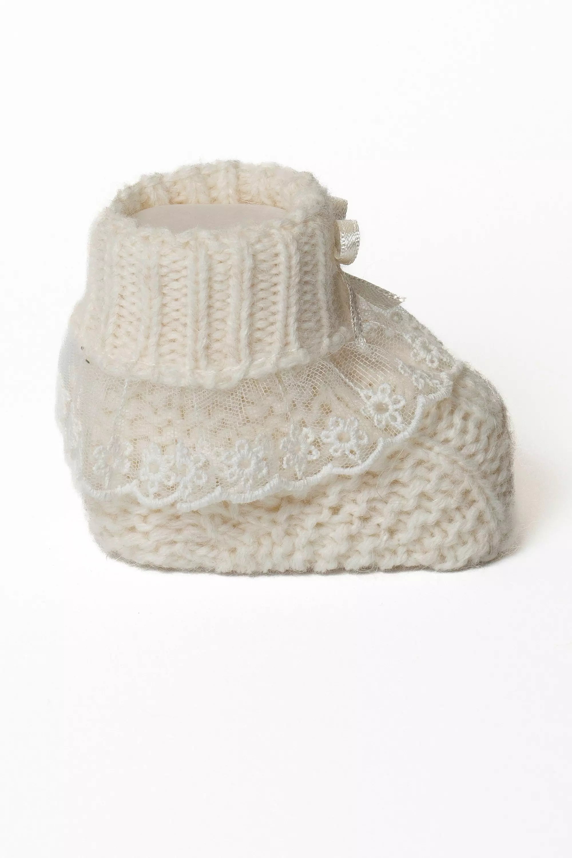 Einzelansicht eines cremeweißen Babystrickschuhs mit breitem Rippbündchen und mehrlagiger Spitzenverzierung.