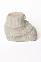 Einzelansicht eines cremeweißen Babystrickschuhs mit breitem Rippbündchen und mehrlagiger Spitzenverzierung.