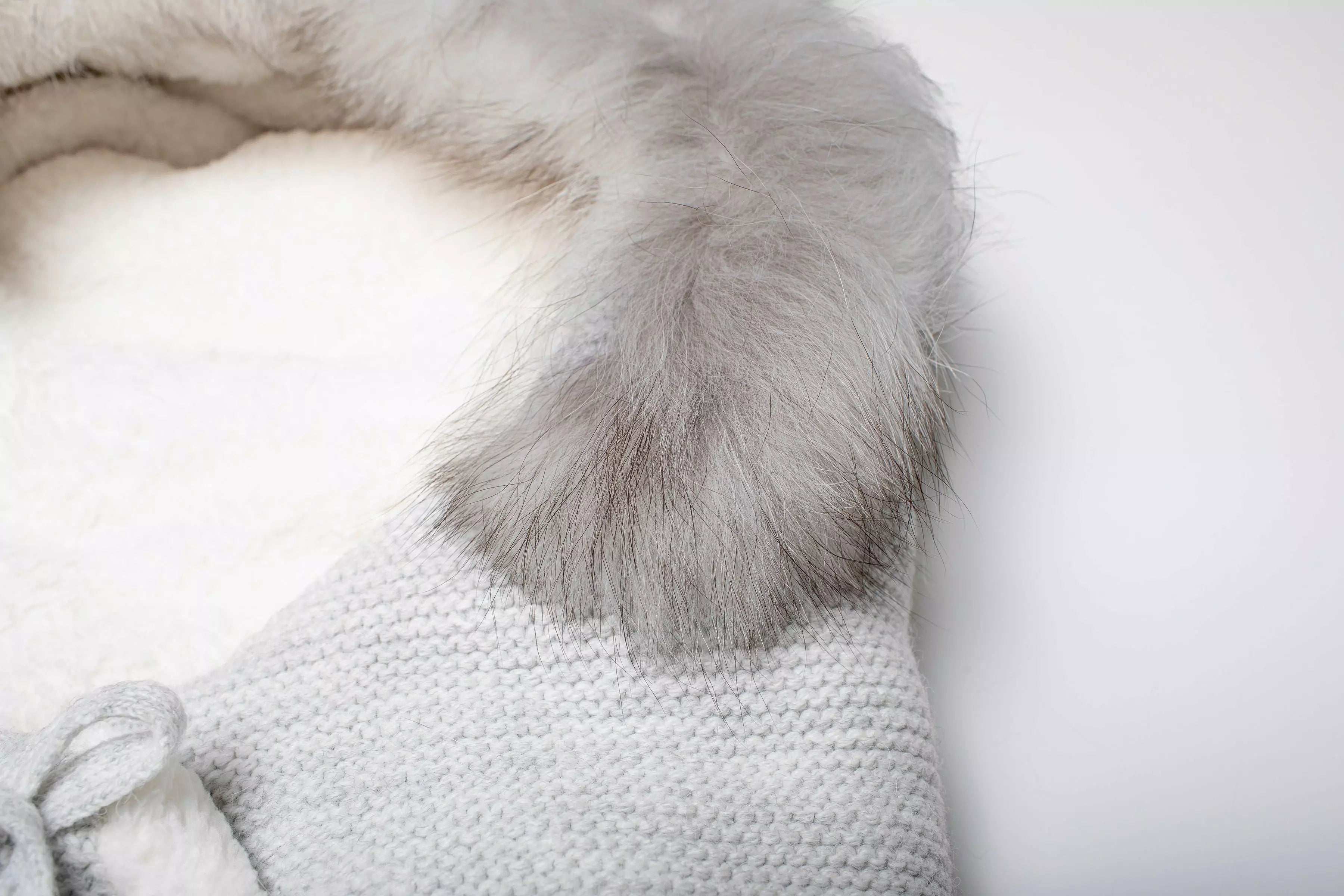 Nahaufnahme des weichen, grauen Fellrands und des flauschigen weißen Innenfutters des Baby-Schlafsacks