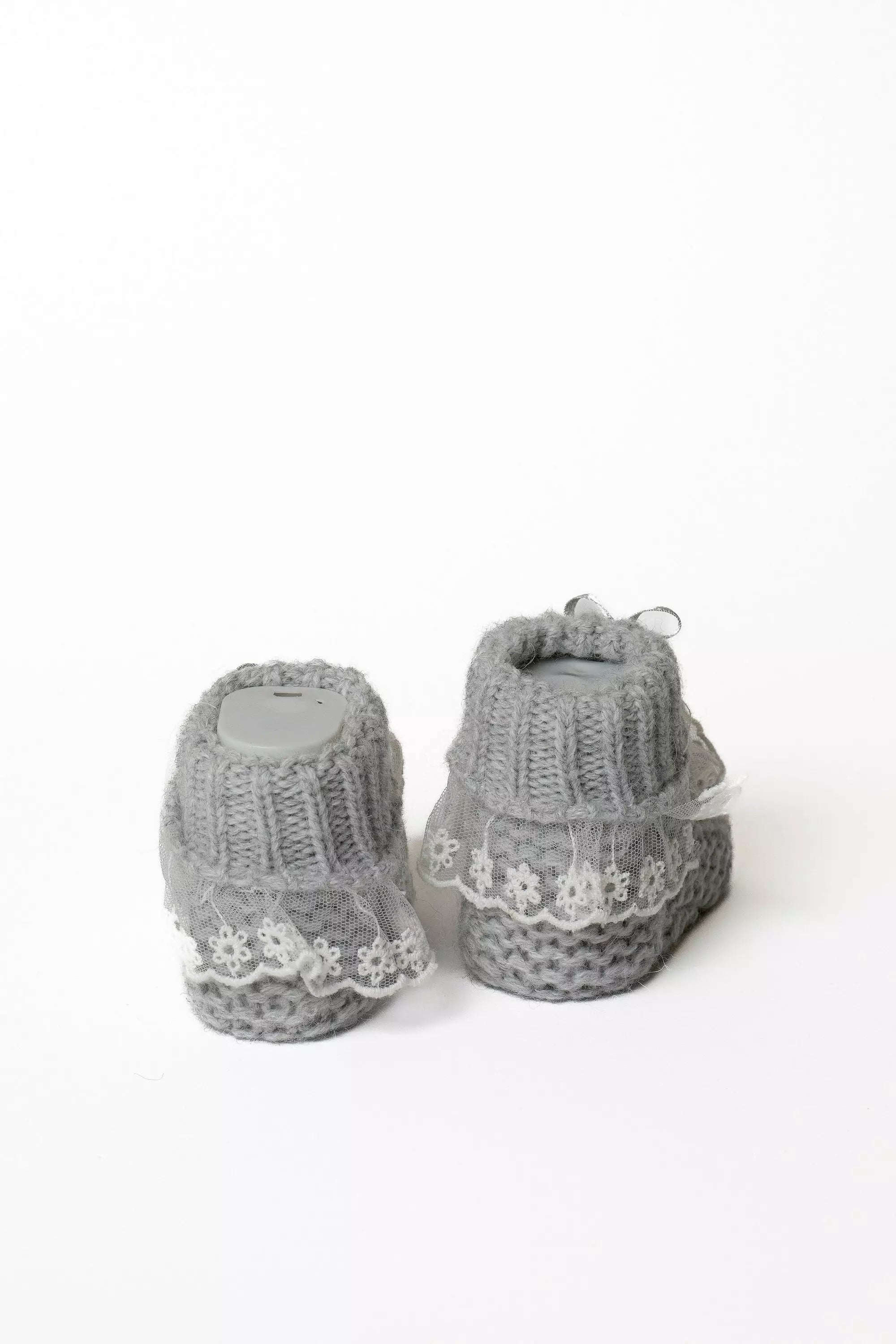 Paar graue Babystrickschuhe von hinten, hebt das dicke Rippbündchen und die helle Spitzeneinfassung hervor.