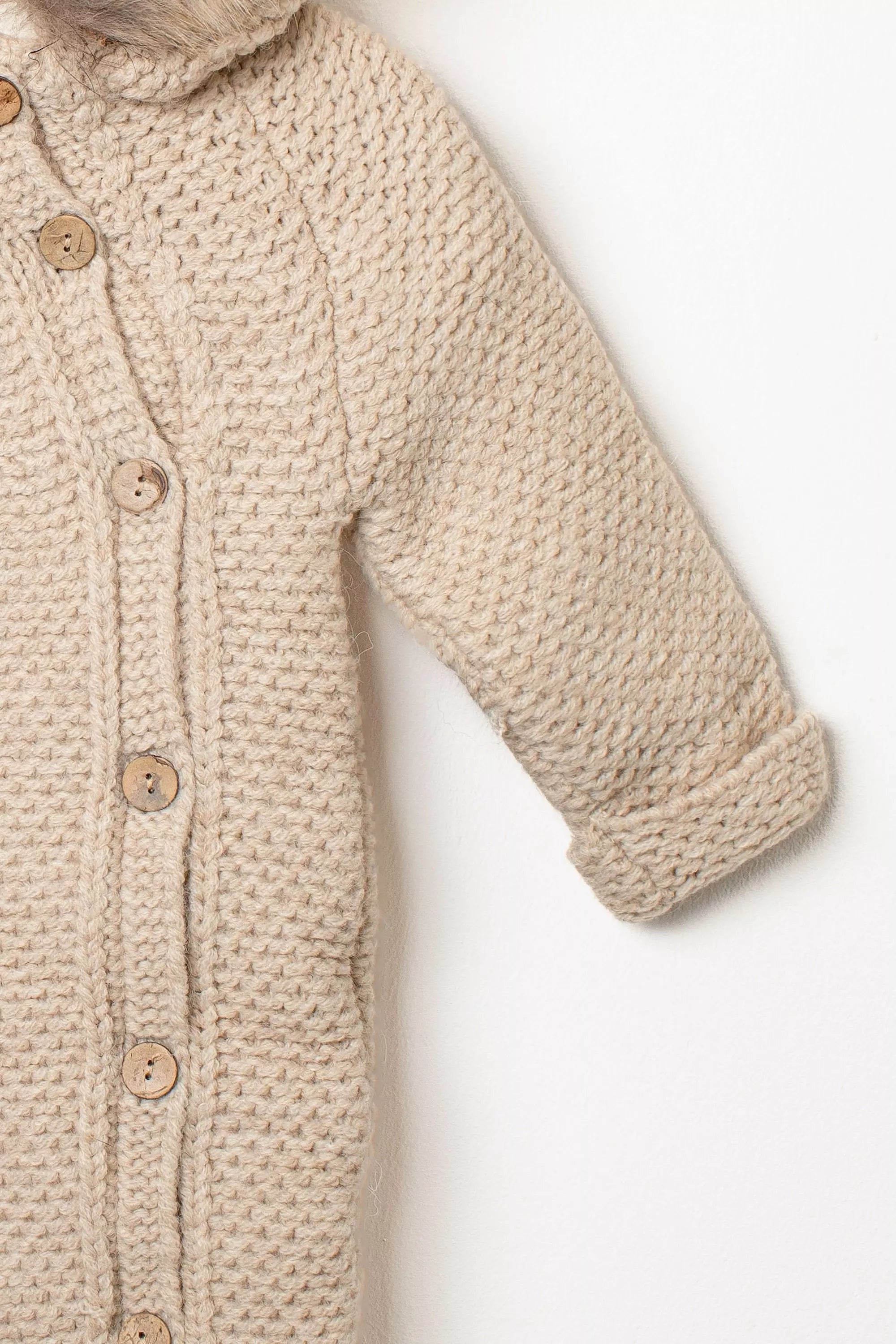 Detailansicht des Ärmels und der Knopfleiste des beigen Baby Strick-Schneeanzugs mit Holzköpfen und umgeschlagenem Strickbündchen.
