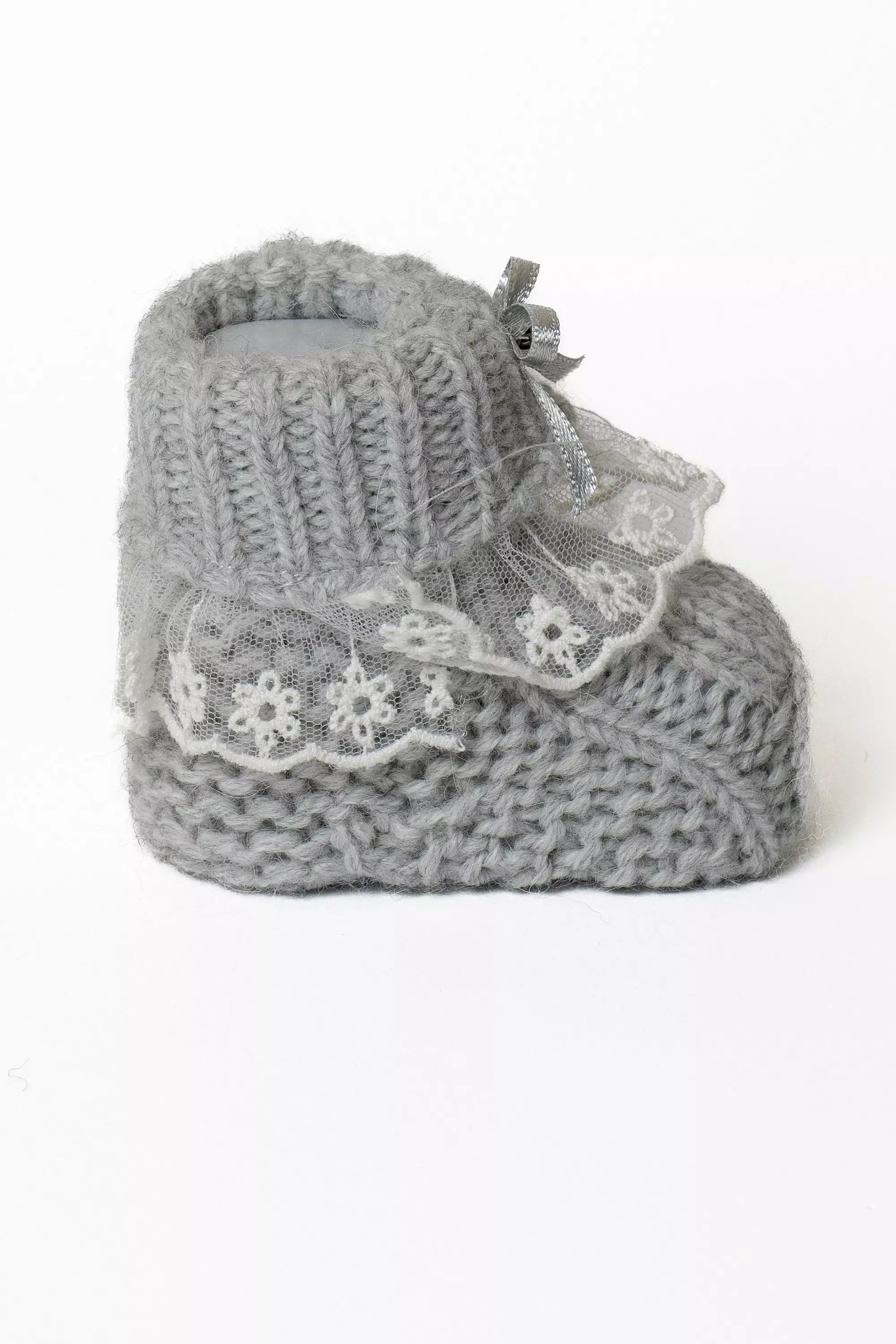 Nahaufnahme eines einzelnen grauen Babystrickschuhs, der das Grobstrickmuster und die dekorative Spitzeneinfassung hervorhebt.