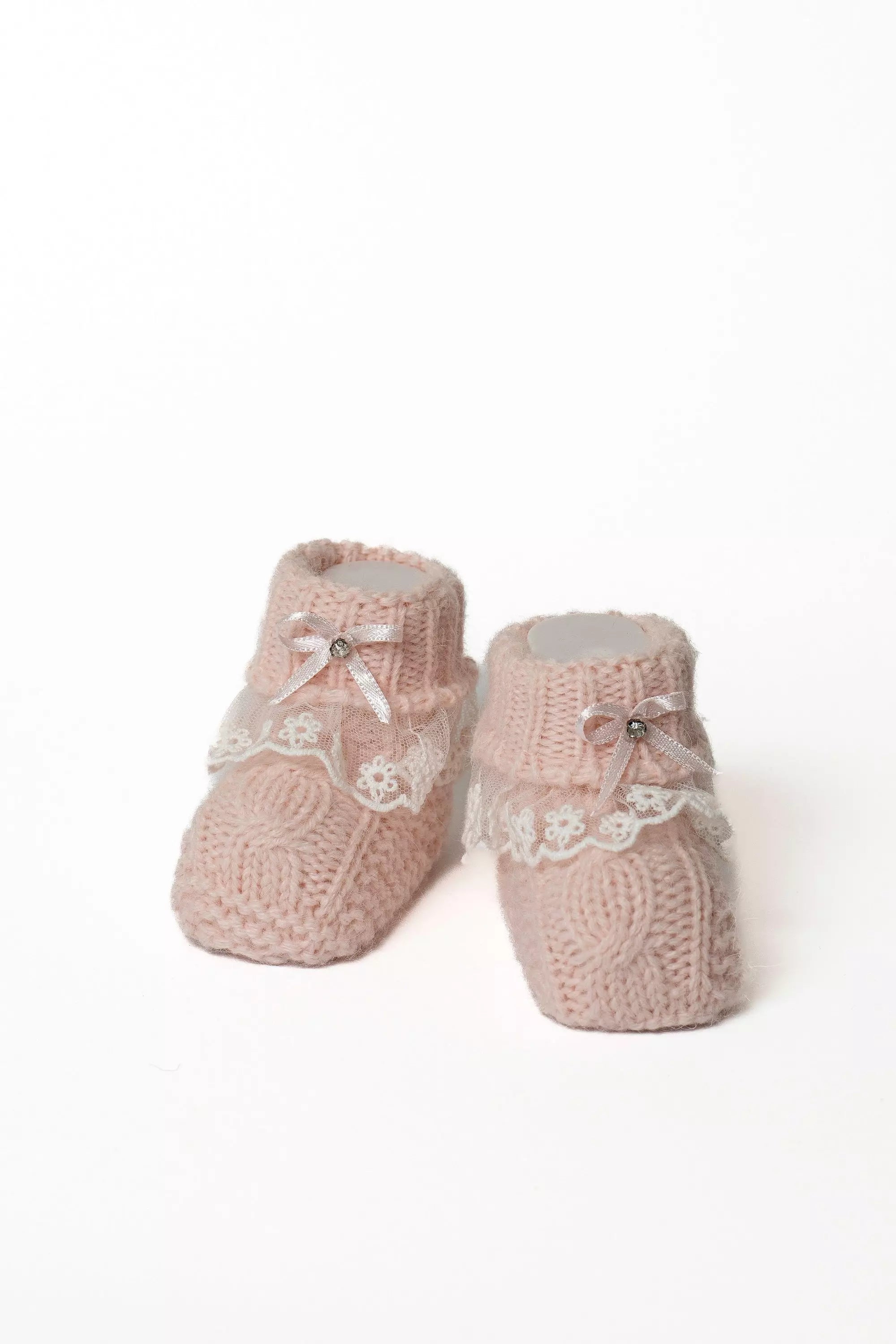 Paar rosa Babystrickschuhe mit Zopfmuster, weißer Spitze und zarter rosa Satinschleife, ideal für Mädchen.