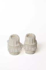 Paar cremeweiße Babystrickschuhe von hinten, mit Rippbündchen und großer weißer Spitzenverzierung.