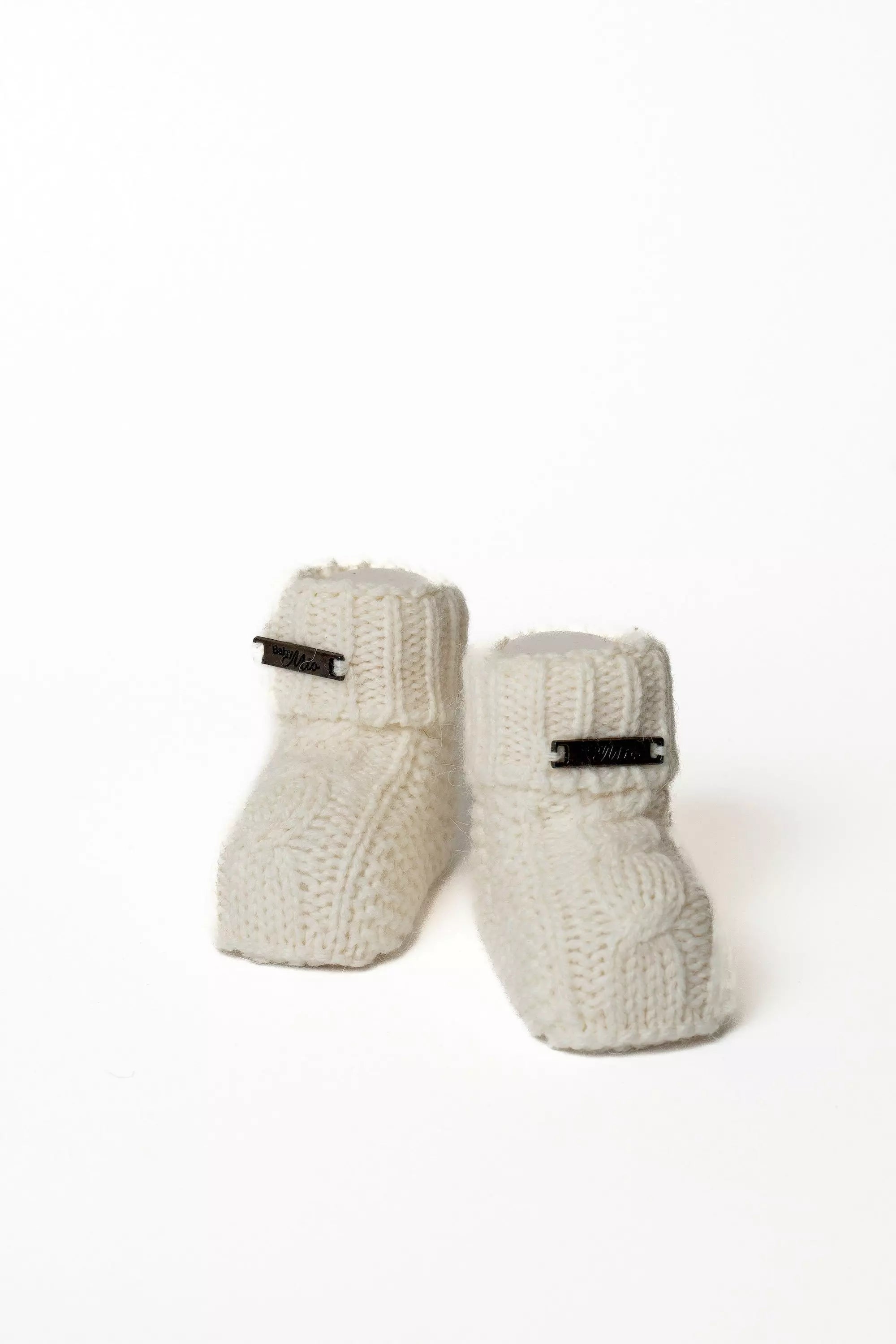 Paar hochwertige weisse Baby Strickschuhe mit Zopfmuster und Label, Warme Strickschuhe