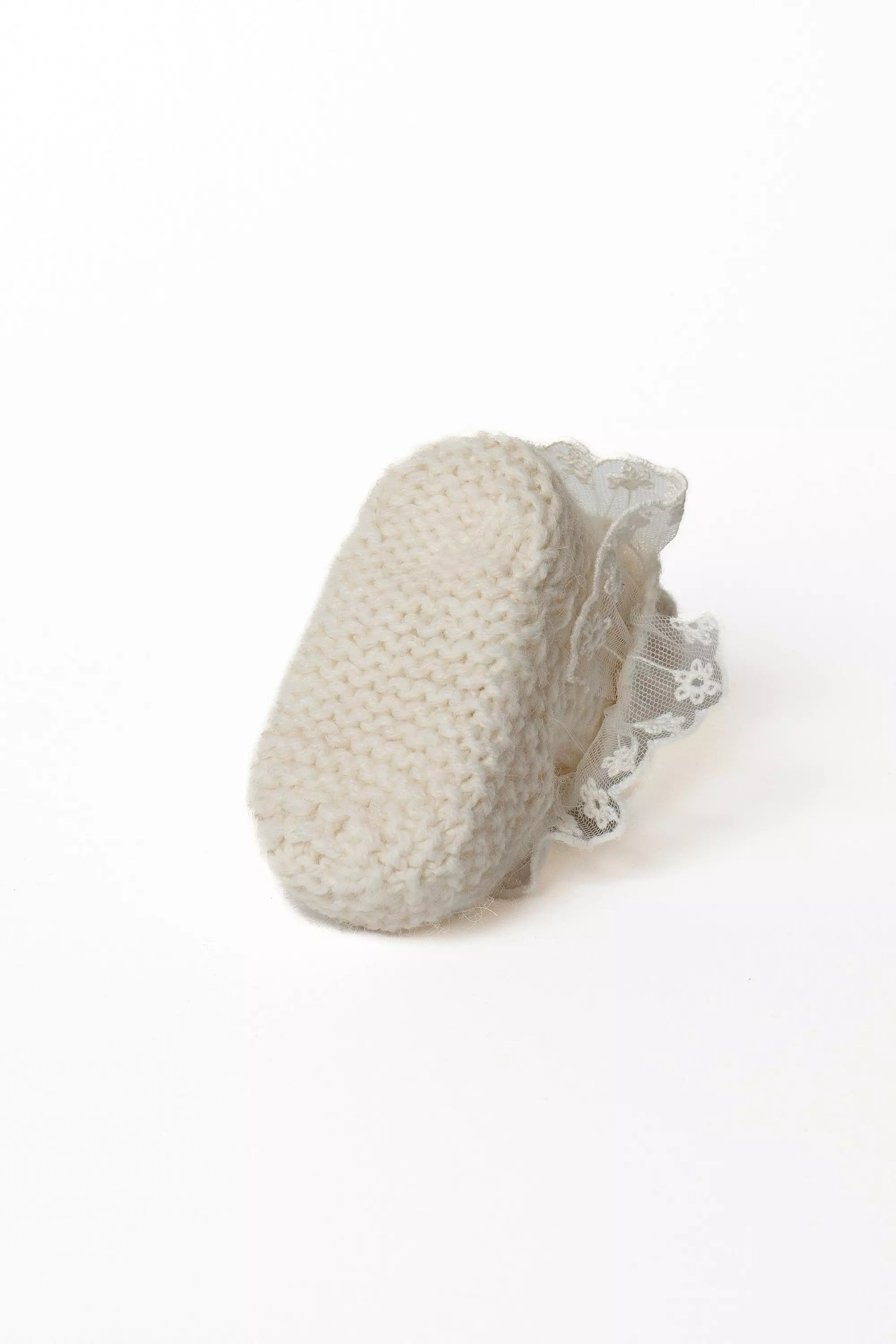 Ansicht der Sohle eines weißen Babystrickschuhs mit Grobstrickmuster und zarter Spitzenborte.